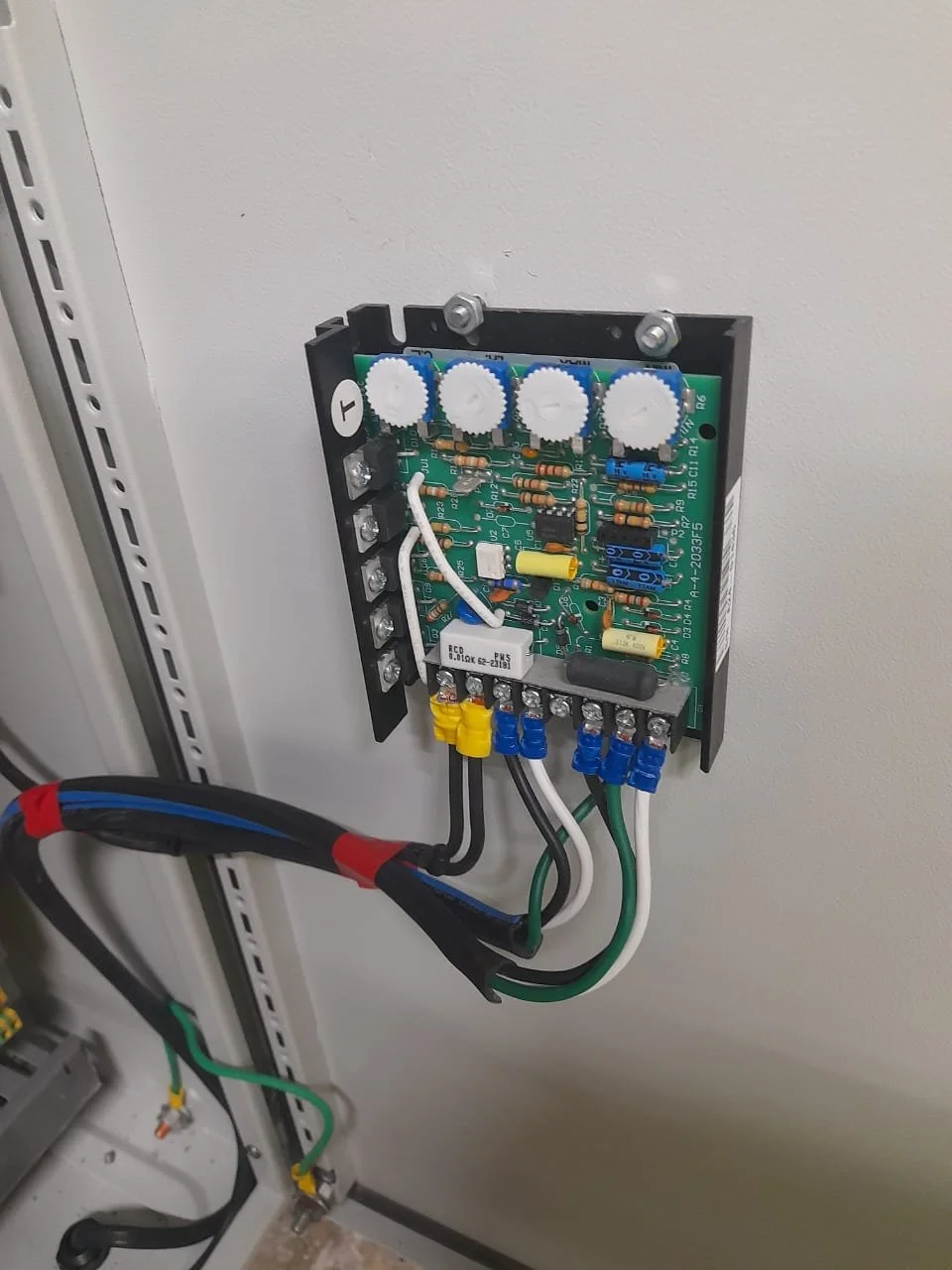 Tarjeta de circuito impreso instalada en una caja eléctrica, con componentes electrónicos, conectores y cables.