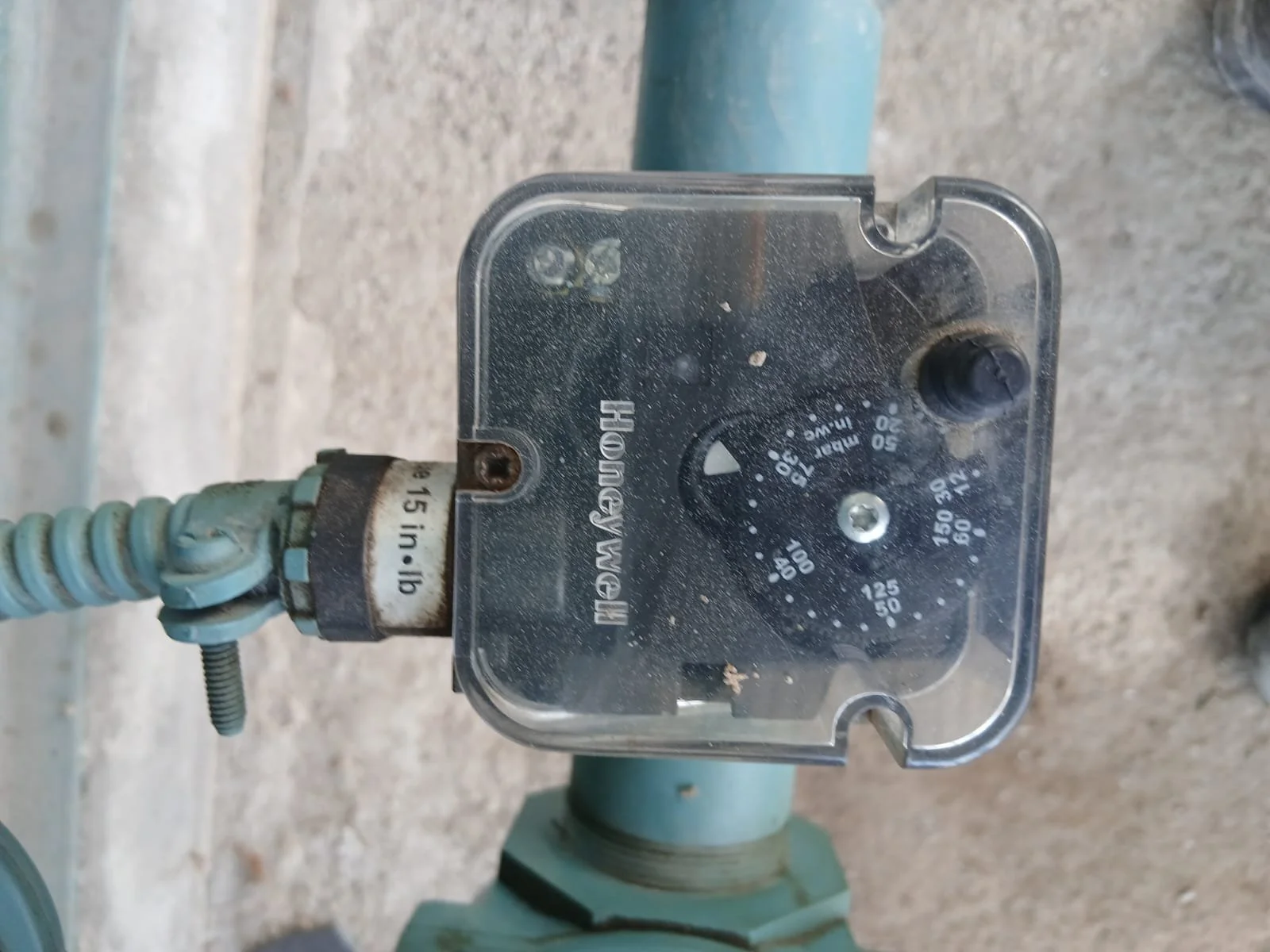 Instrumento de medición de agua con dial, conectado a una tubería, con display de temperaturas y presiones, en un ambiente externo.