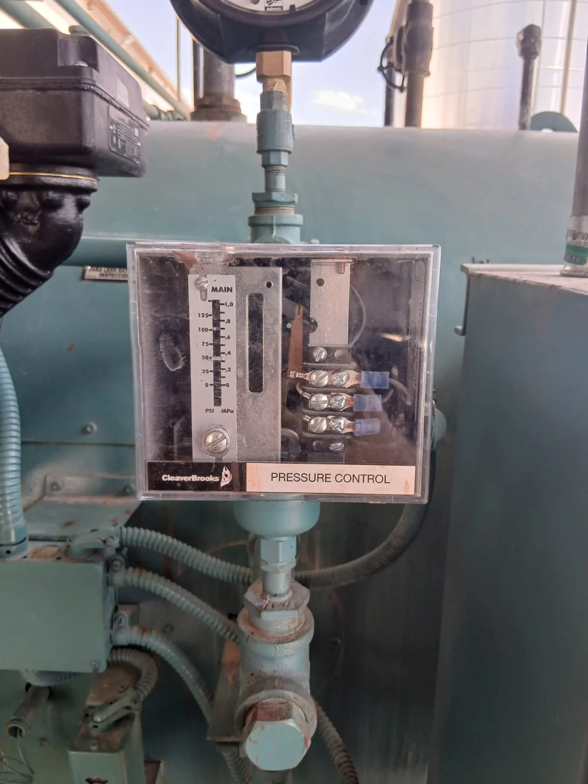 Control de presión en un equipo industrial, con manómetro y válvula, en un entorno de maquinaria y tuberías.