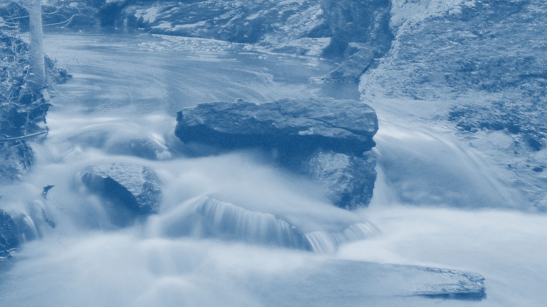 Flowing river with rocks and stones, surrounded by rocky banks and cliffs.