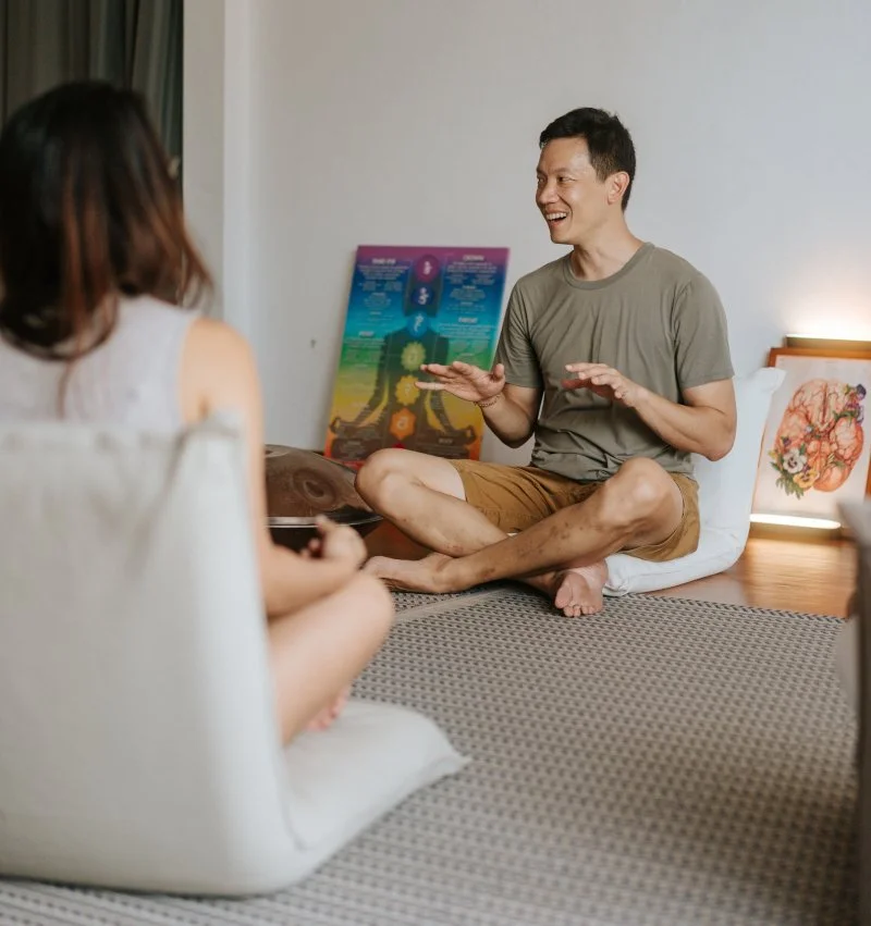 Instructor seated and teaching a workshop to a class with a handpan and photos of chakra and the brain in the background