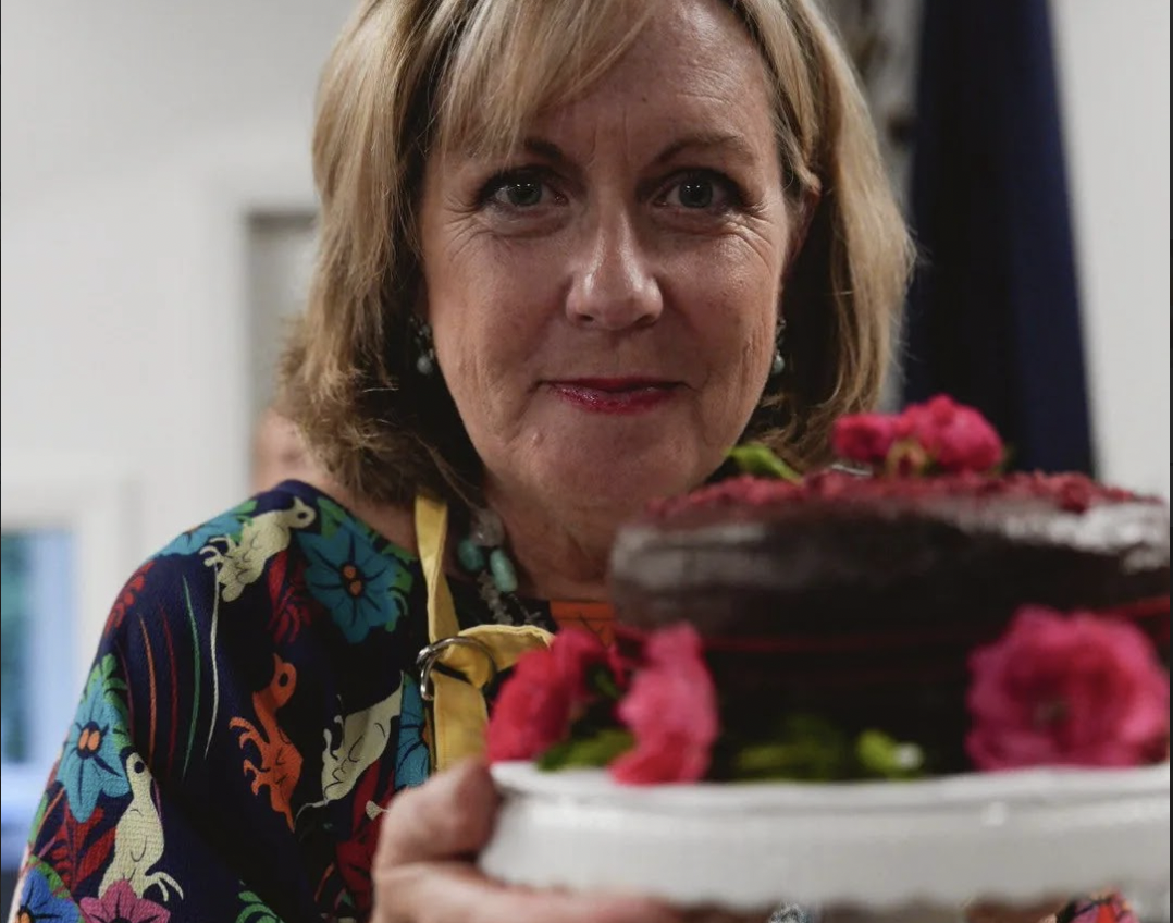 A woman holding a cake decorated with pink flowers and raspberries.