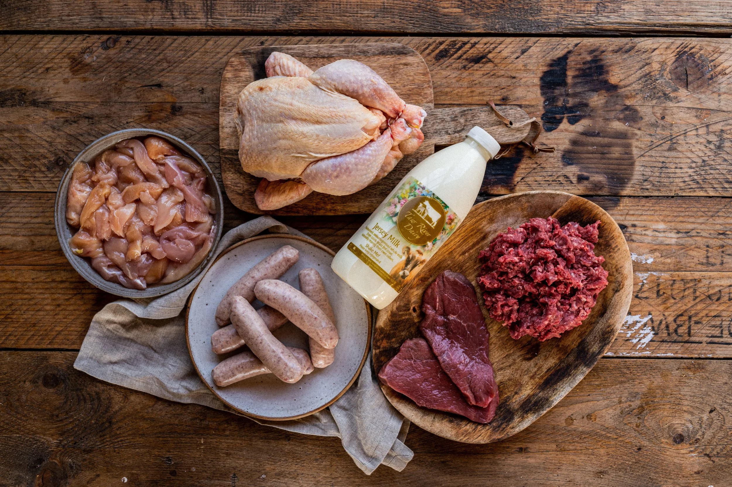 Raw chicken, sausages, ground beef, veal, chicken breast, and milk on a wooden table.