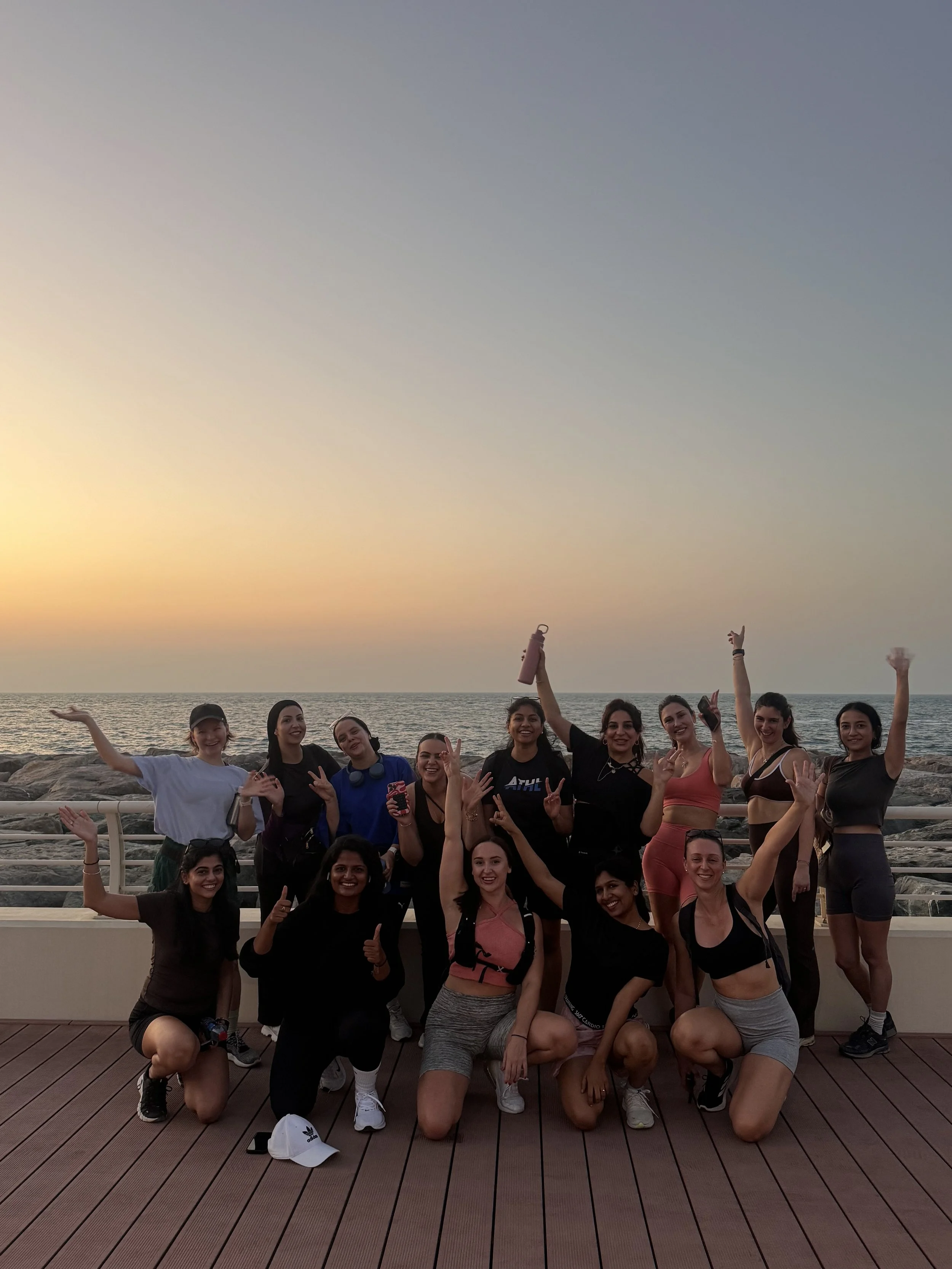 Group of six people riding horses in a desert landscape at sunset with minimal vegetation and distant buildings.