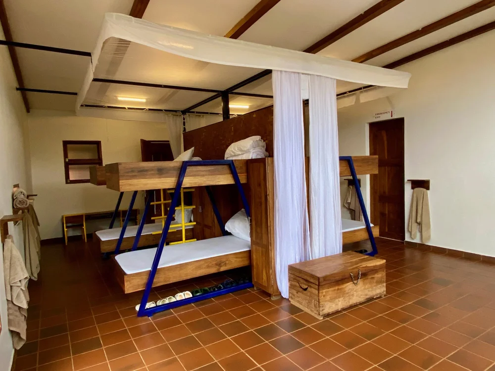 Dorm bedroom with wooden bunk beds, mosquito nets and storage trunks
