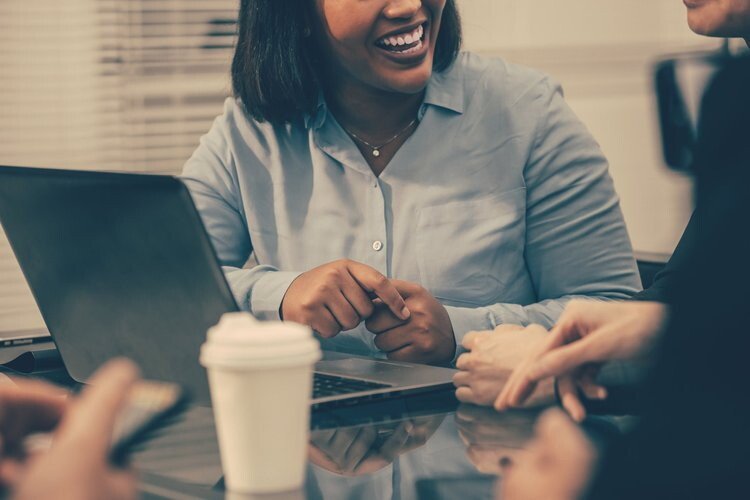Women smiling and talking in a meeting with laptops and a coffee cup on the table.