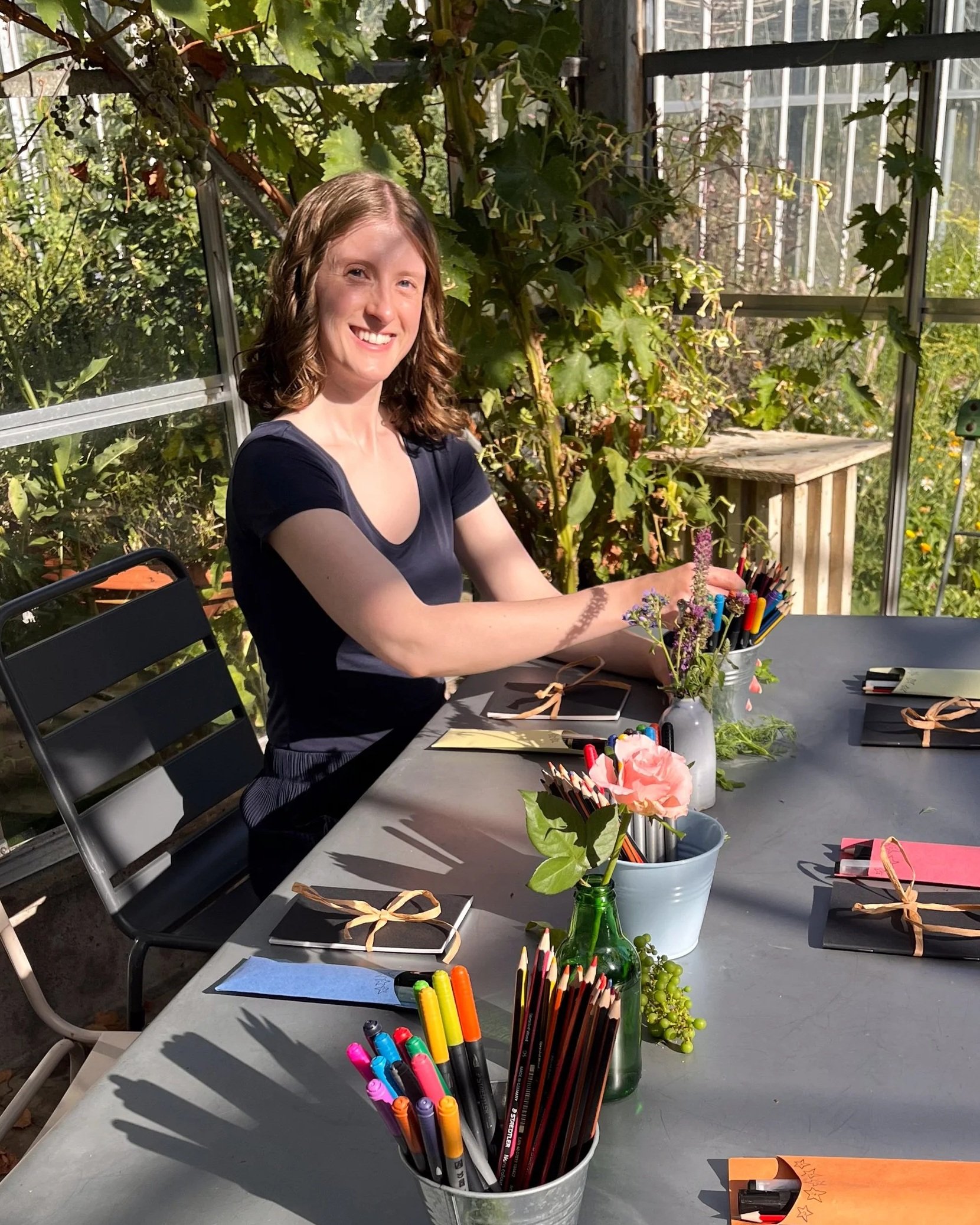 Host Bethan sat at a table with sketchbooks wrapped with ribbon, pen pots and mini floral arrangements.