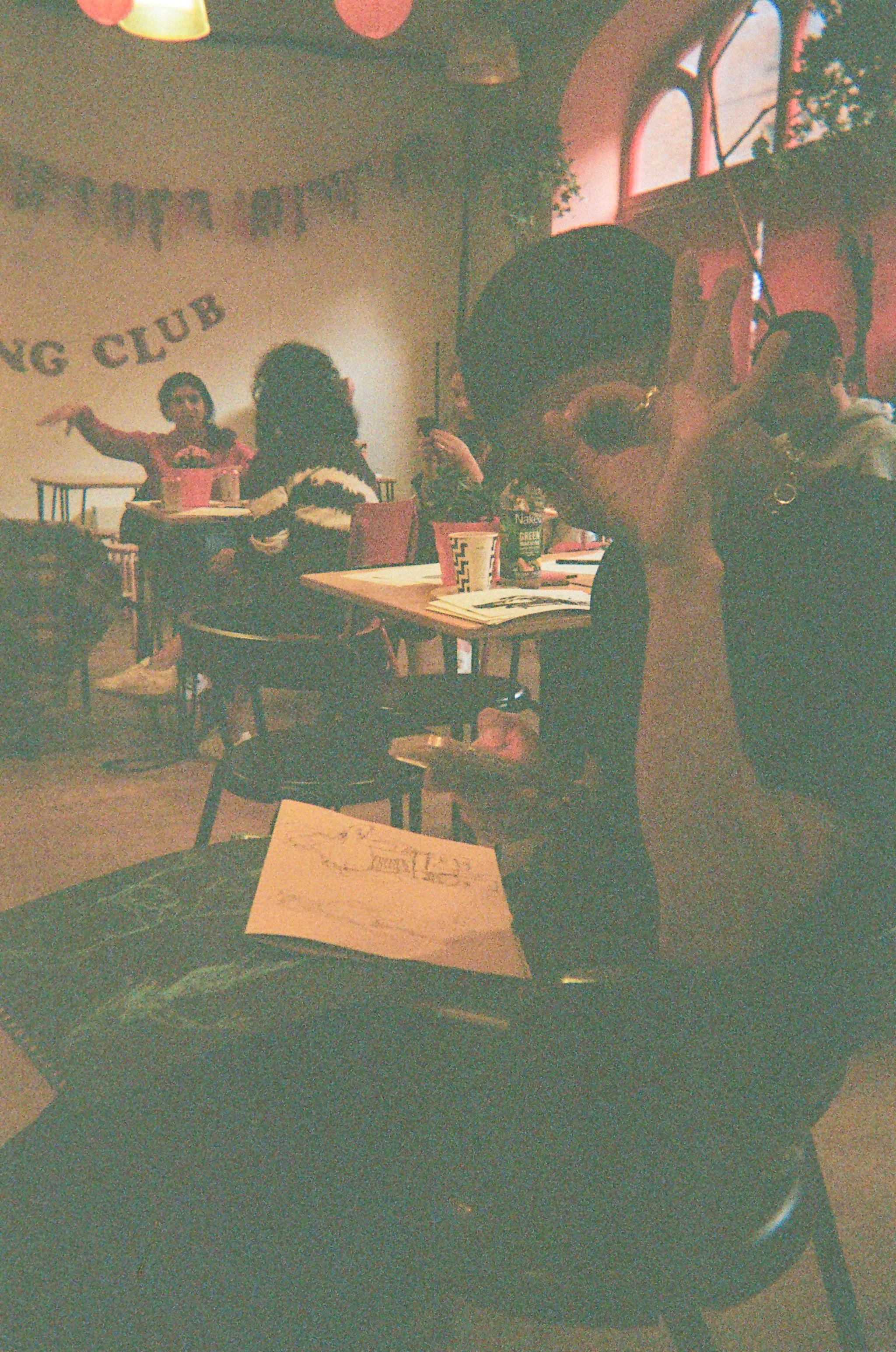 Drawing Club attendee posing for the camera, making a circle with their finger and looking through it at the camera. Sketches on their lap.