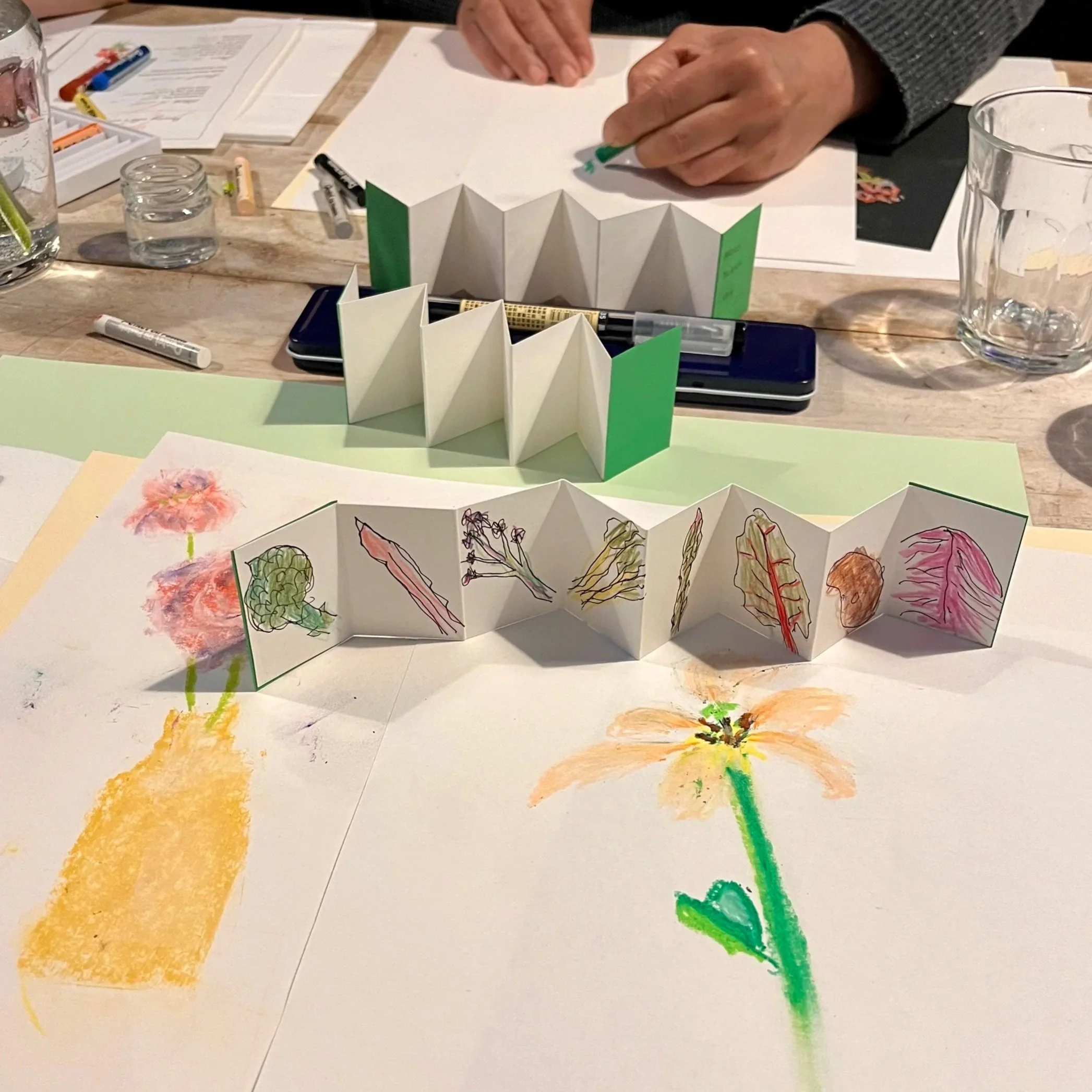 Mini concertina books filled with drawings of tiny vegetables. A pair of hands sketching.