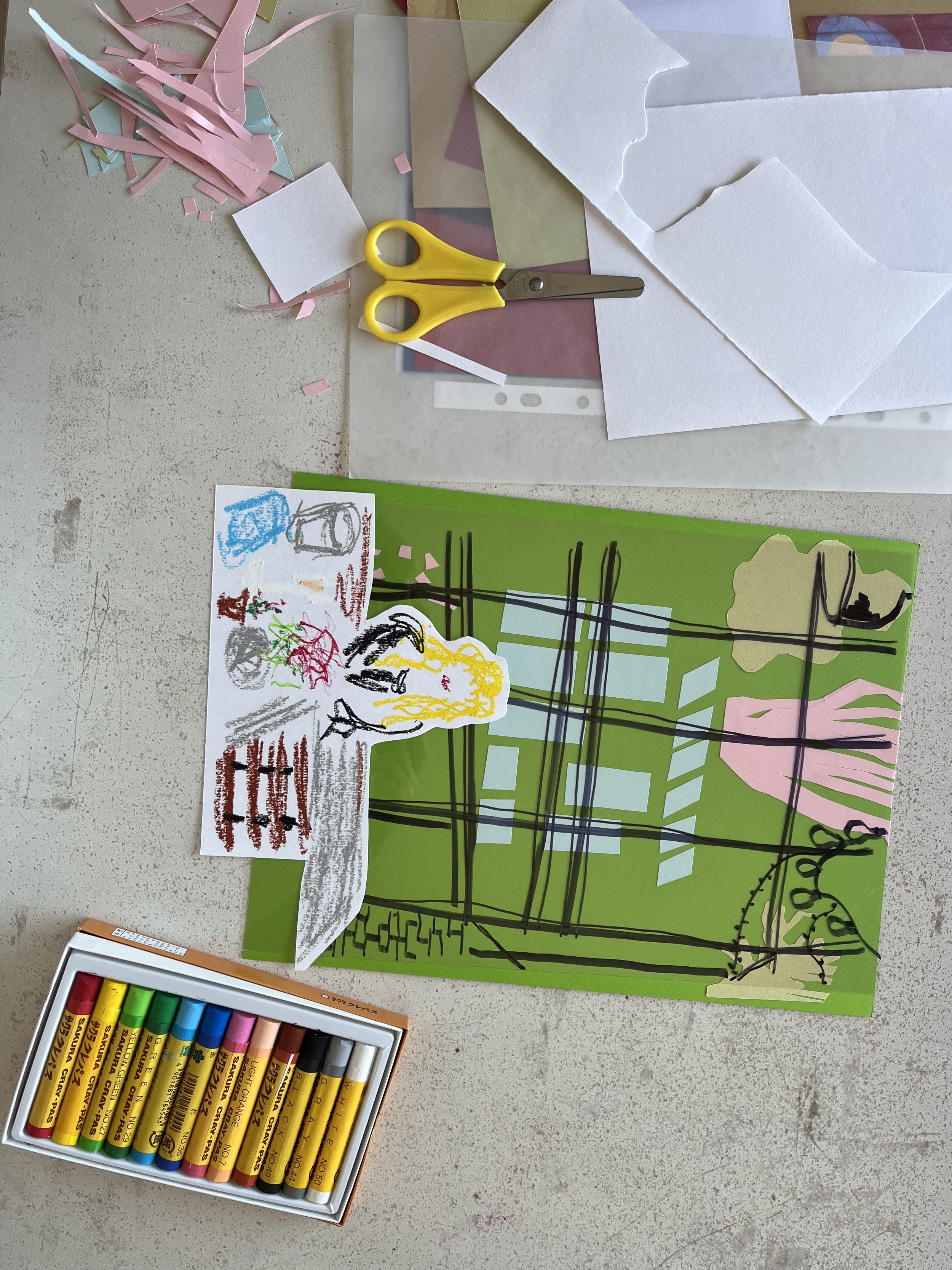 Layered drawing of a person and beyond a window: collaged colour card background, acetate and sharpie layer for glass representation and figure drawn sat a table in oil pastels. Pair of scissors and pack of oil pastels on the white table beside it.