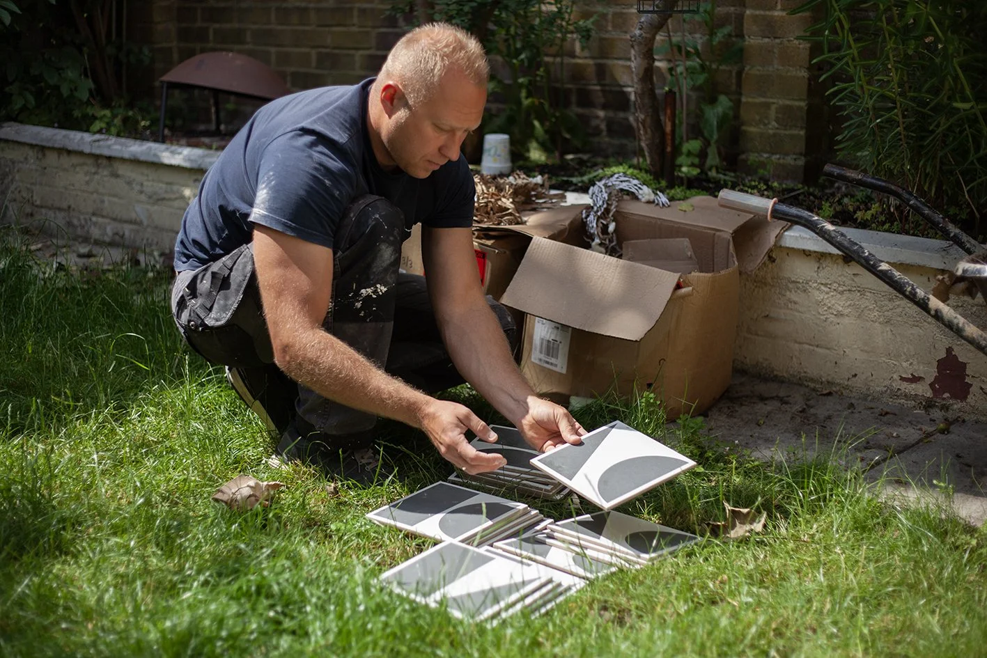 Checkatrade work. Harringay, London. Tomazs, at work as a bathroom renovator. Tomazs looks through a box of tiles in the customer's garden. 2025.