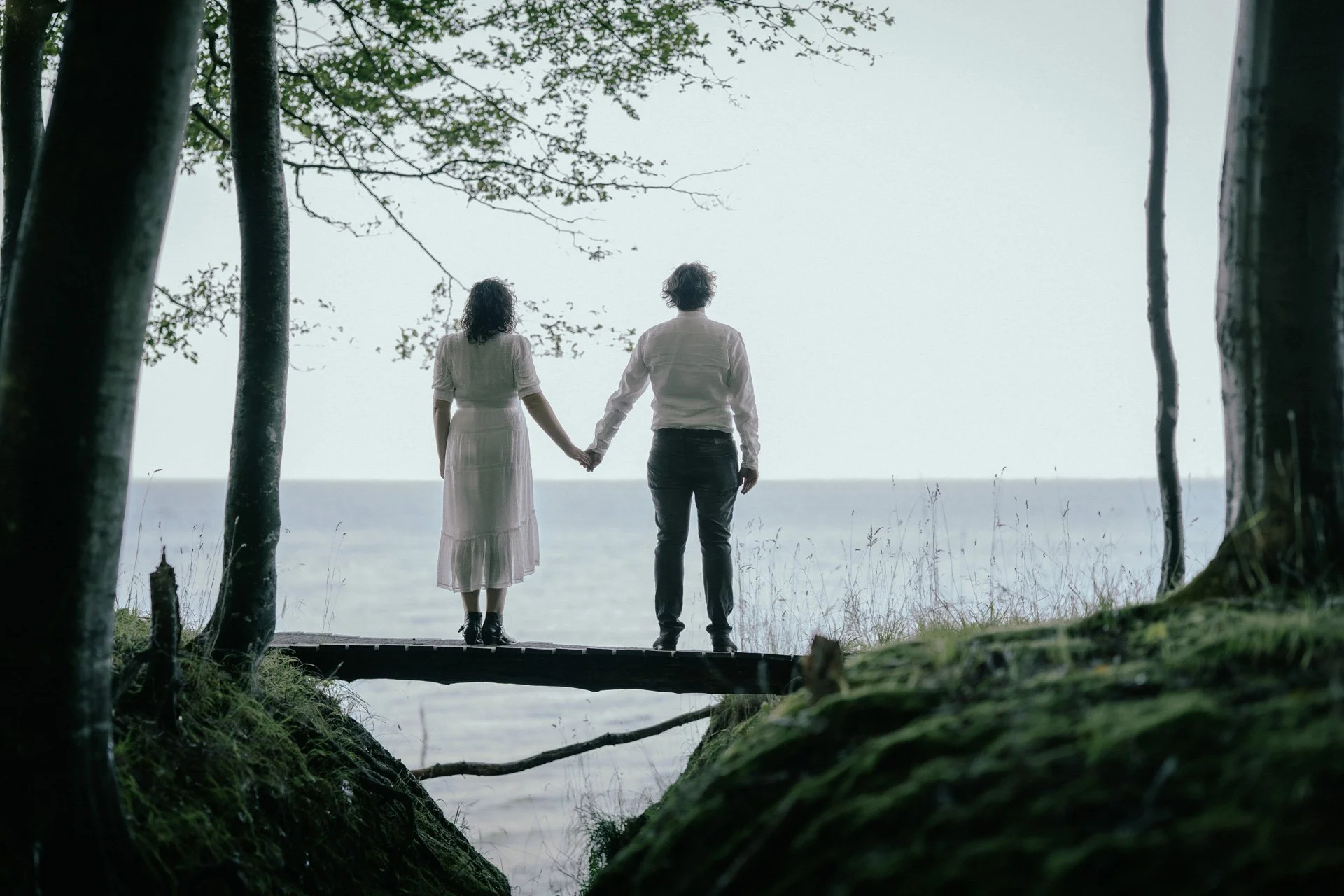Ein Paar hält Händchen am Ufer des Meeres, umgeben von Bäumen.