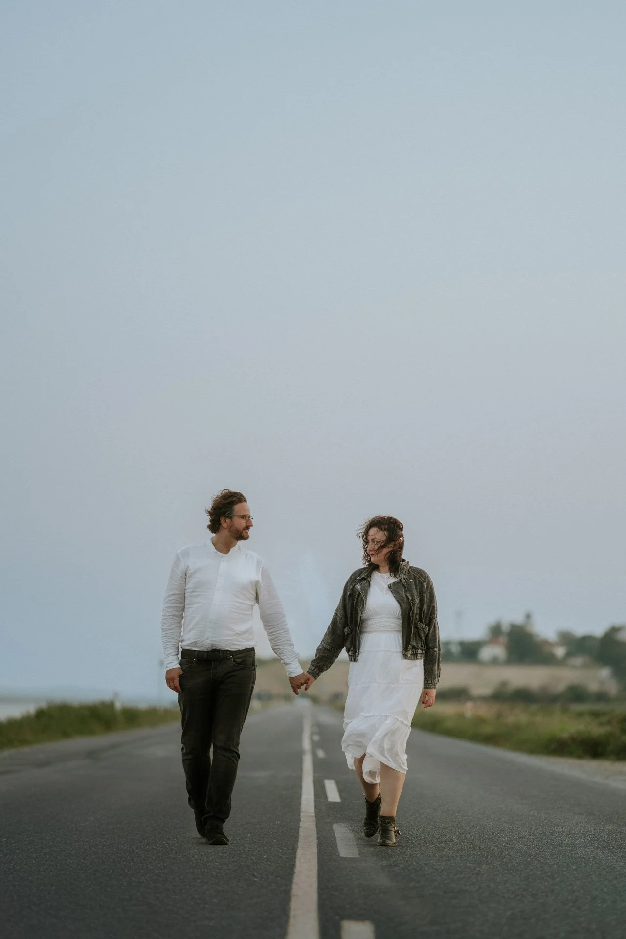 Ein Mann und eine Frau laufen Hand in Hand auf einer leeren Straße bei bewölktem Himmel.