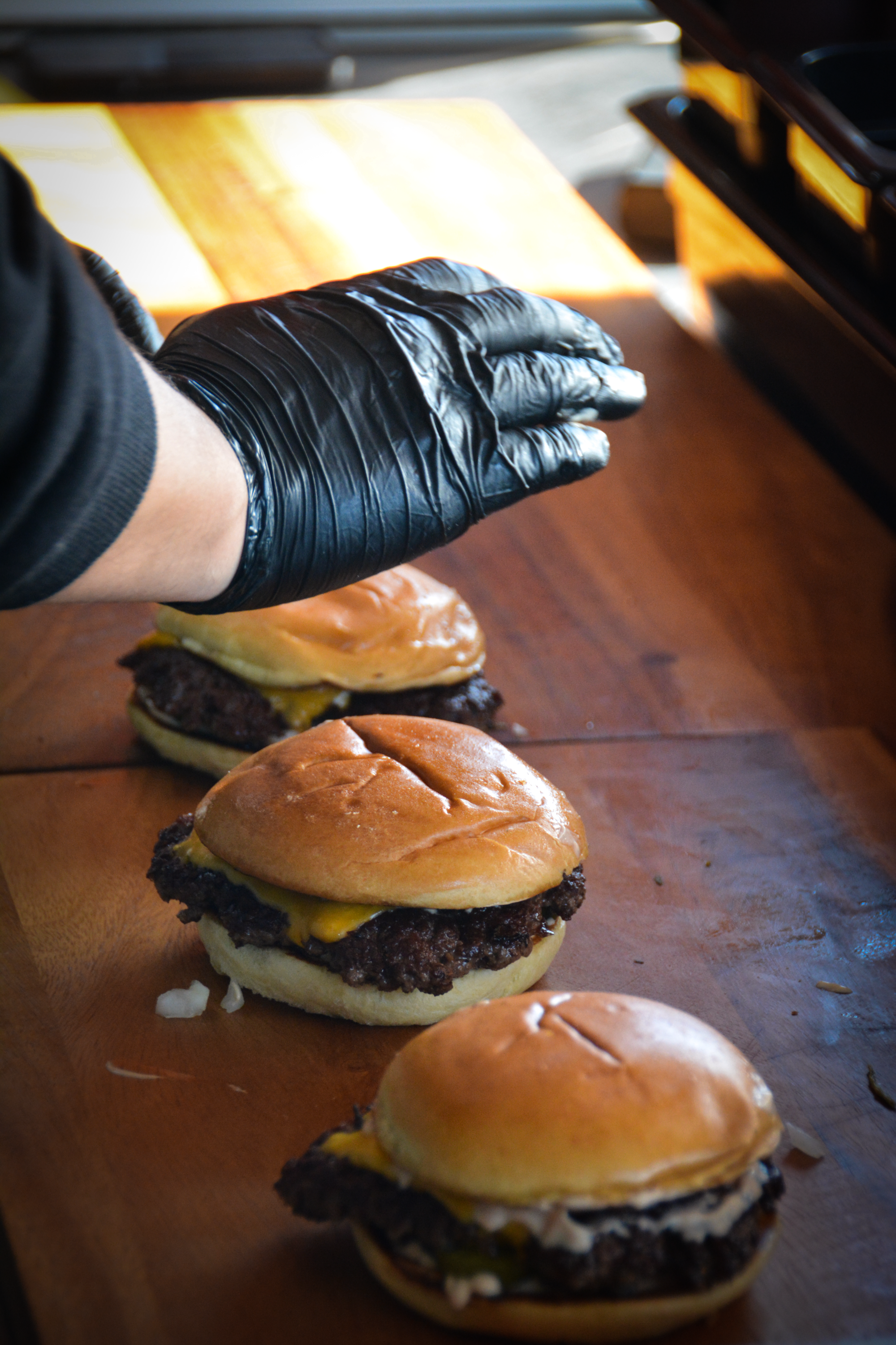 En person med sort handske klargør tre burgere på en træbord under sollys │Smash Burger Truck│Copenhagen│ København