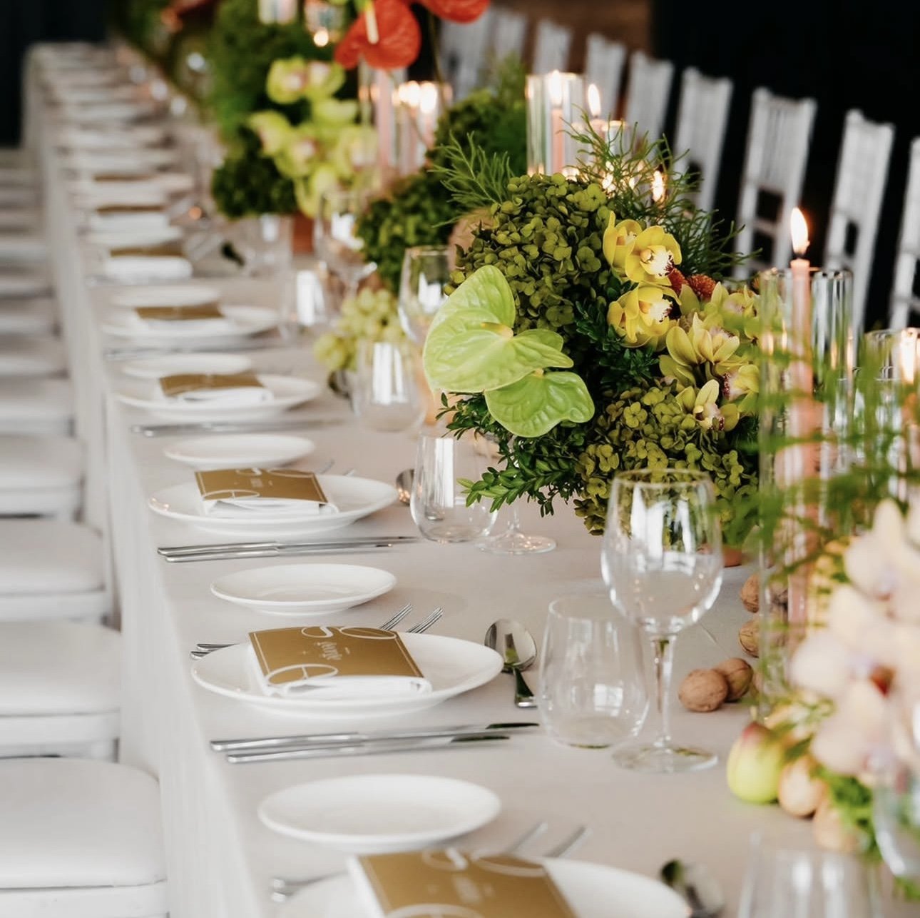 Elegant banquet table decorated with green and yellow floral arrangements, candles, wine glasses, and white plates, set for a formal event.