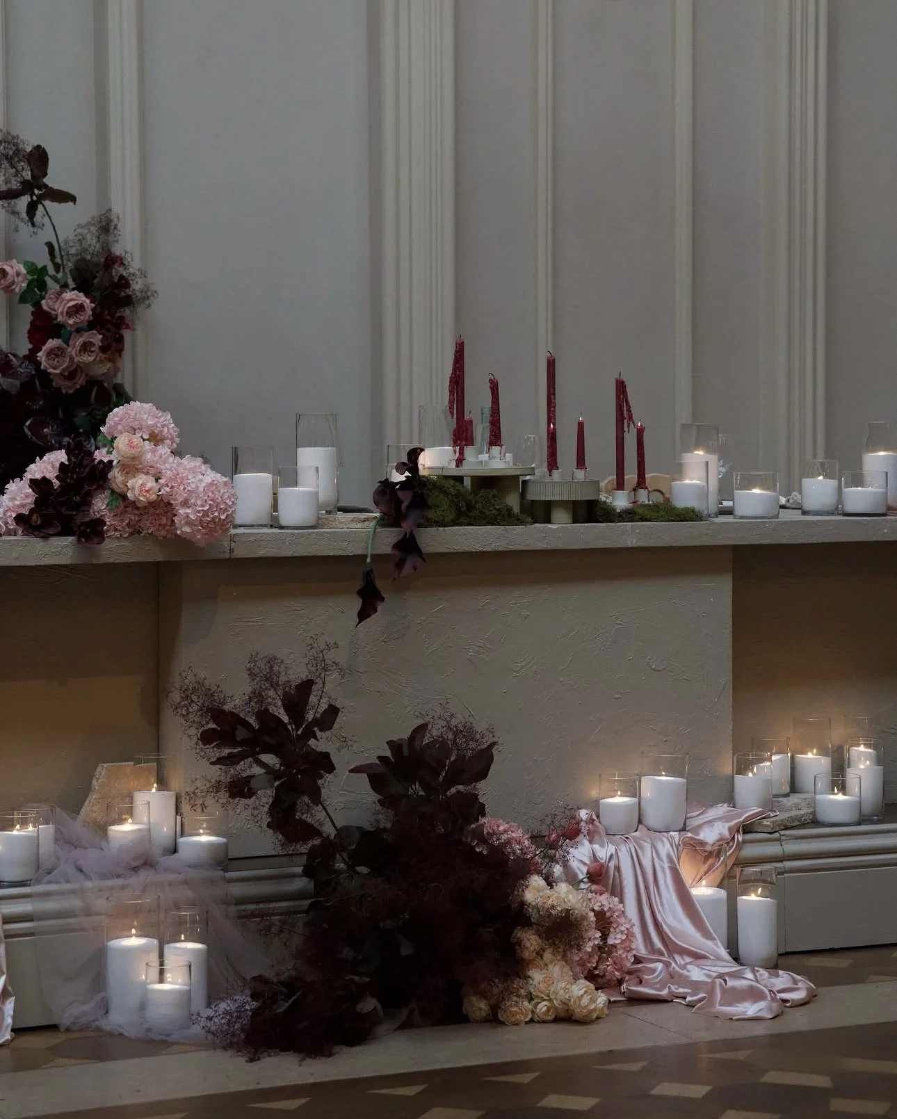 Table decorated with pink and burgundy flowers, white candles, and red candles, set for a special occasion or celebration.