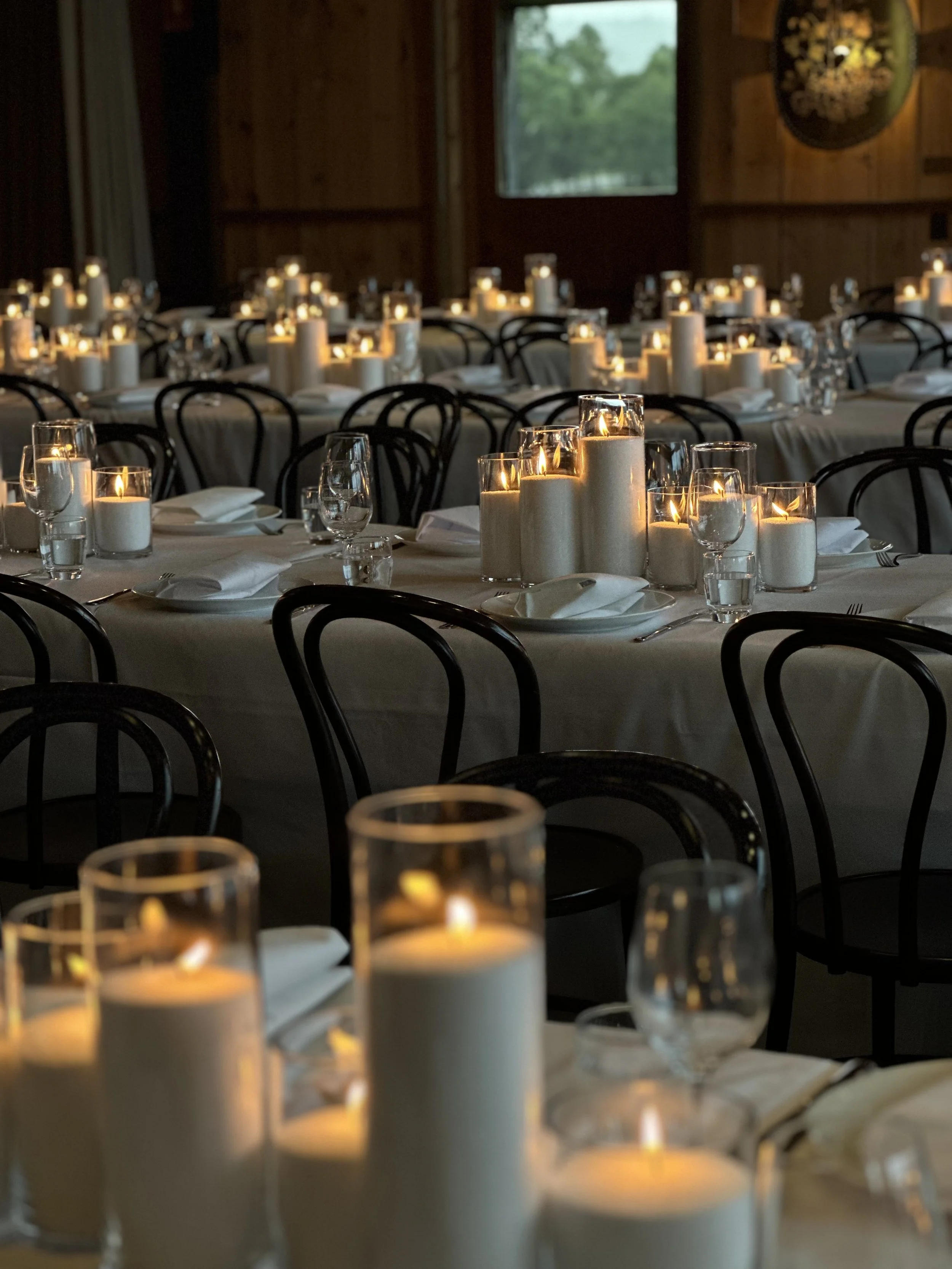 Interior of a dimly lit banquet hall with tables decorated with white tablecloths, candles, and glassware for a formal event.