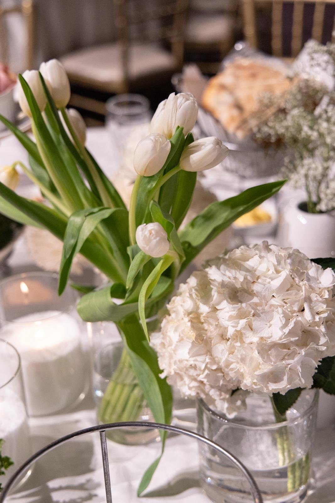White tulips and white hydrangeas in glass vases on a table.