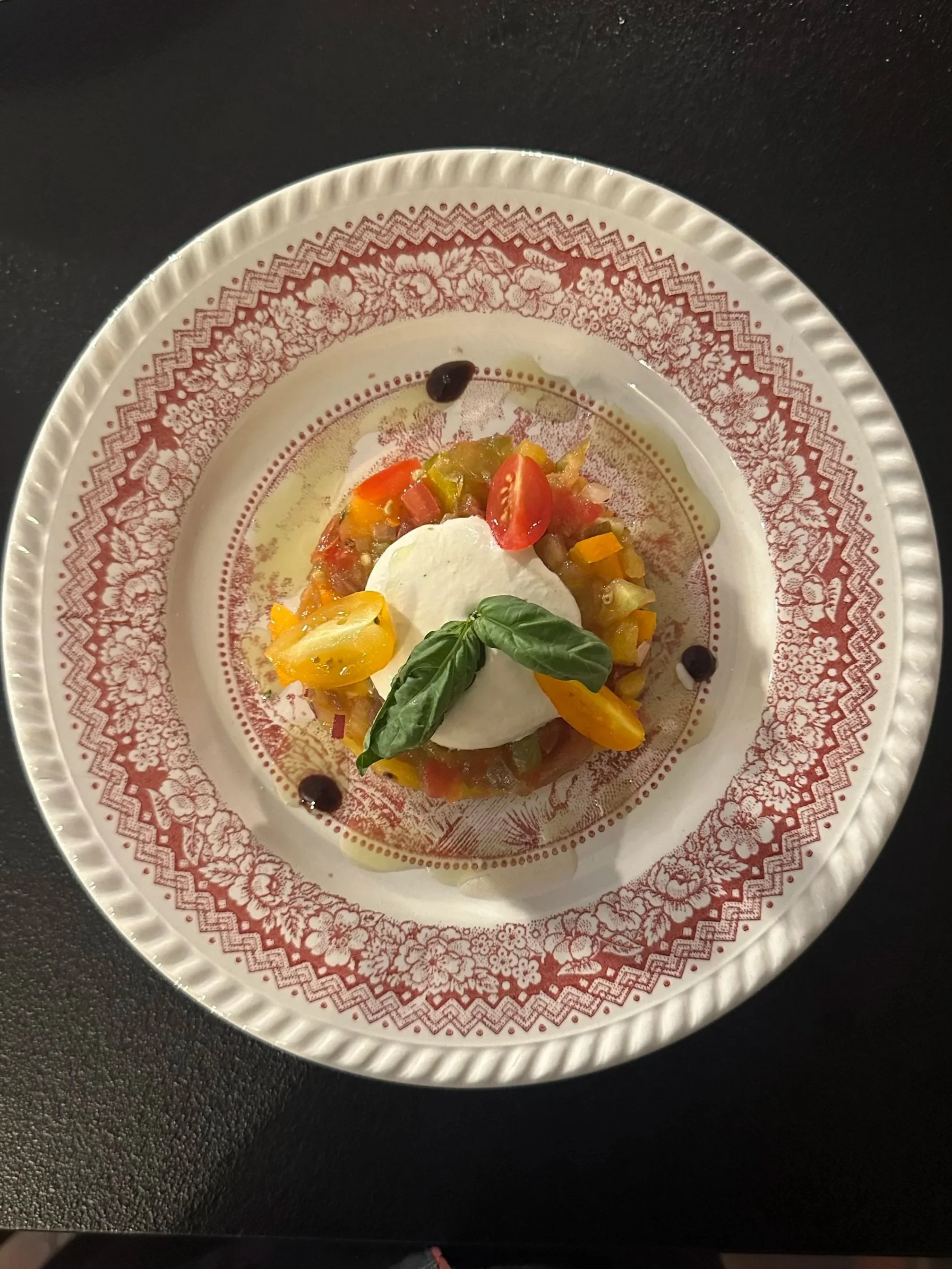 Assiette de tartare de légumes avec une boule de fromage frais, garnie de basilic, tomates cerises, et sauce balsamique