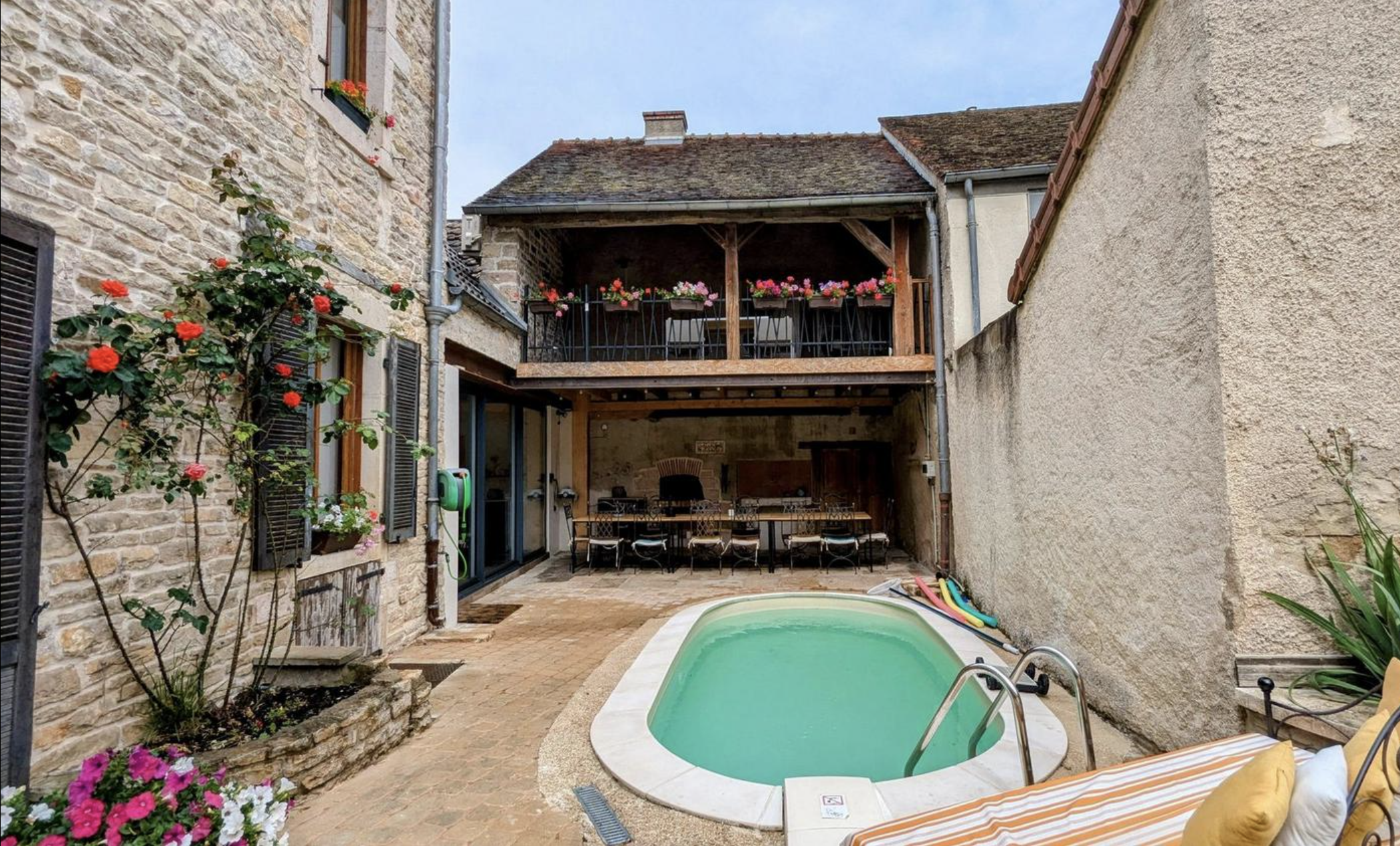 cour arrière avec jacuzzi, fleurs colorées, maison en pierre et balcon en bois