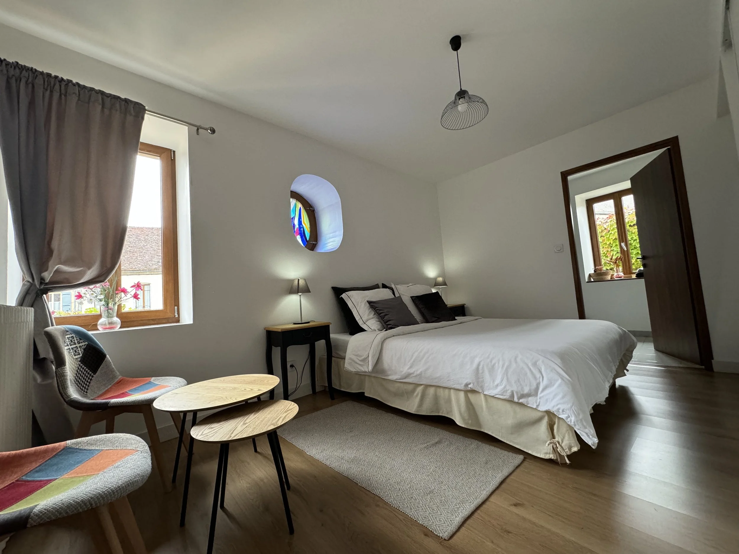 Chambre lumineuse avec lit double, fenêtres avec rideaux, petits meubles, plantes et décoration