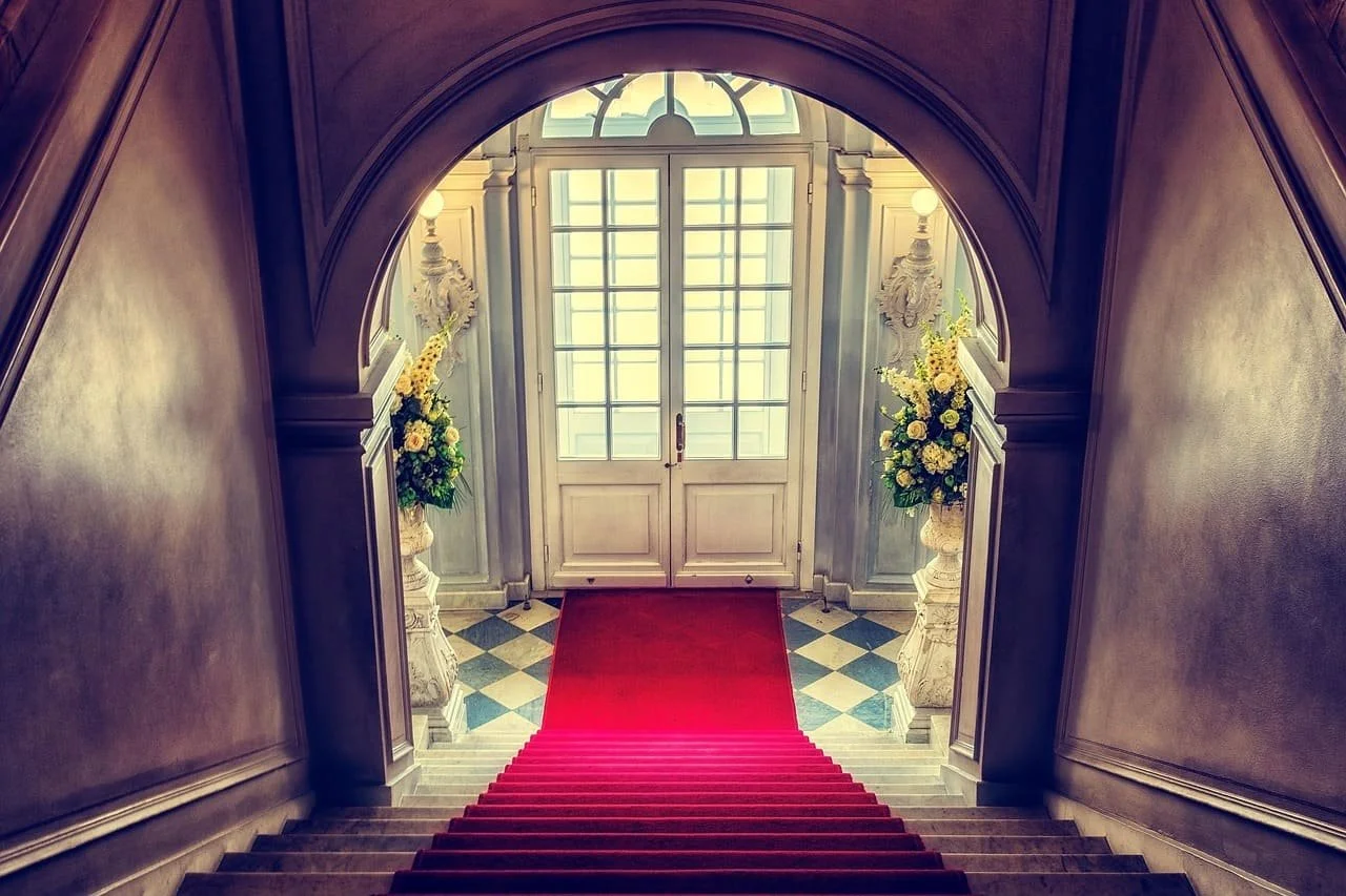 Escalier avec tapis rouge menant à une porte en verre, décorée de vases avec des fleurs, dans une entrée élégante