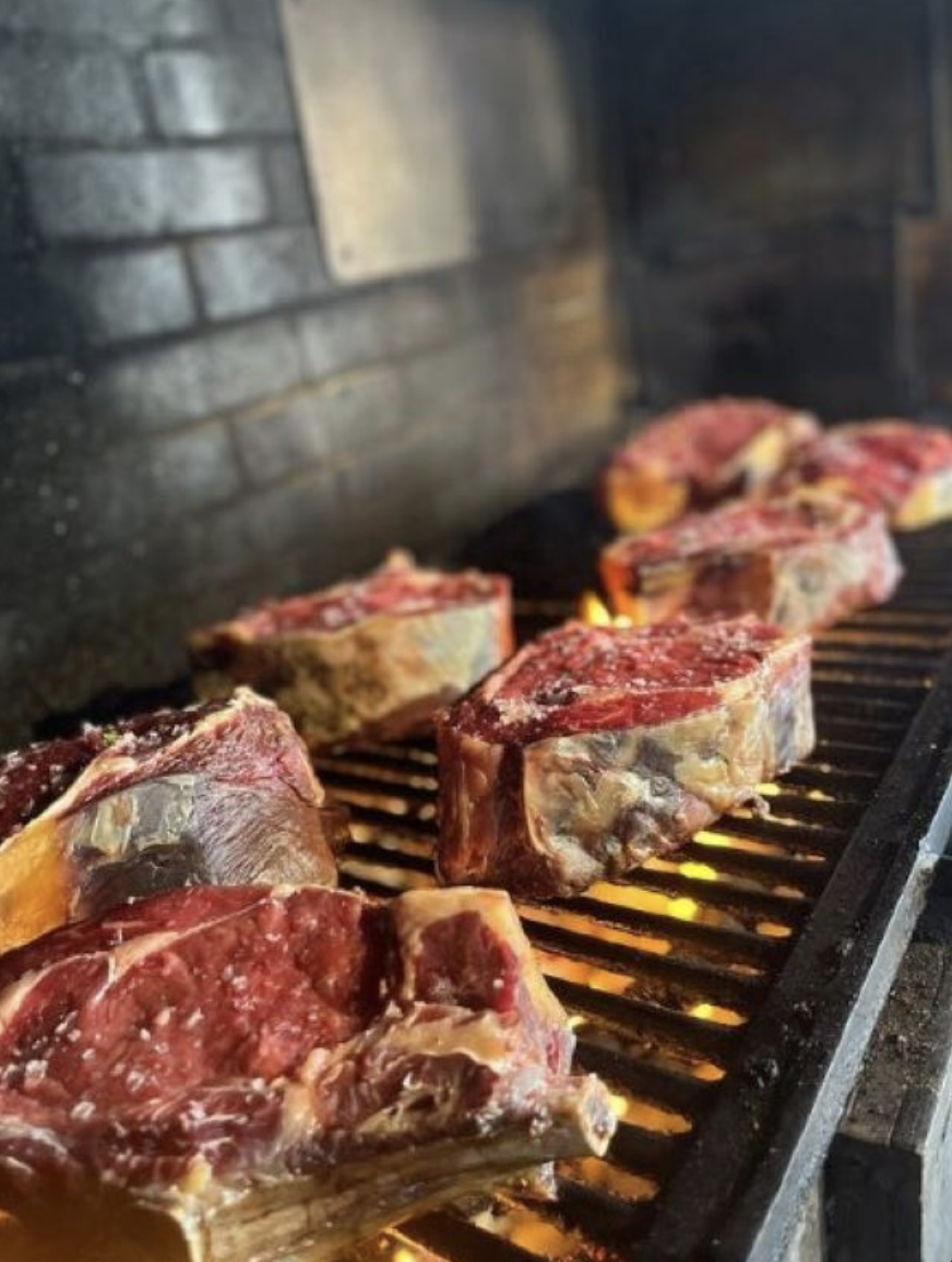 Gros morceaux de viande en train de cuire sur un grill de barbecue avec des flammes en dessous.