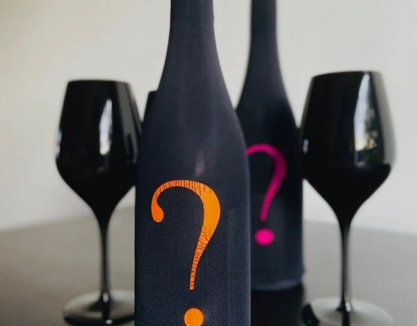 Deux bouteilles noires avec un point d'interrogation orange sur l'une d'elles, flanquées de deux verres à vin noirs. L'arrière-plan est flou.