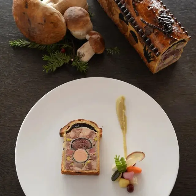 Gâteau roulé au chocolat avec des champignons à gauche et un plat de foie gras en haut. Le gâteau est présenté sur une assiette blanche avec une décoration de foie gras et de légumes en dessous.