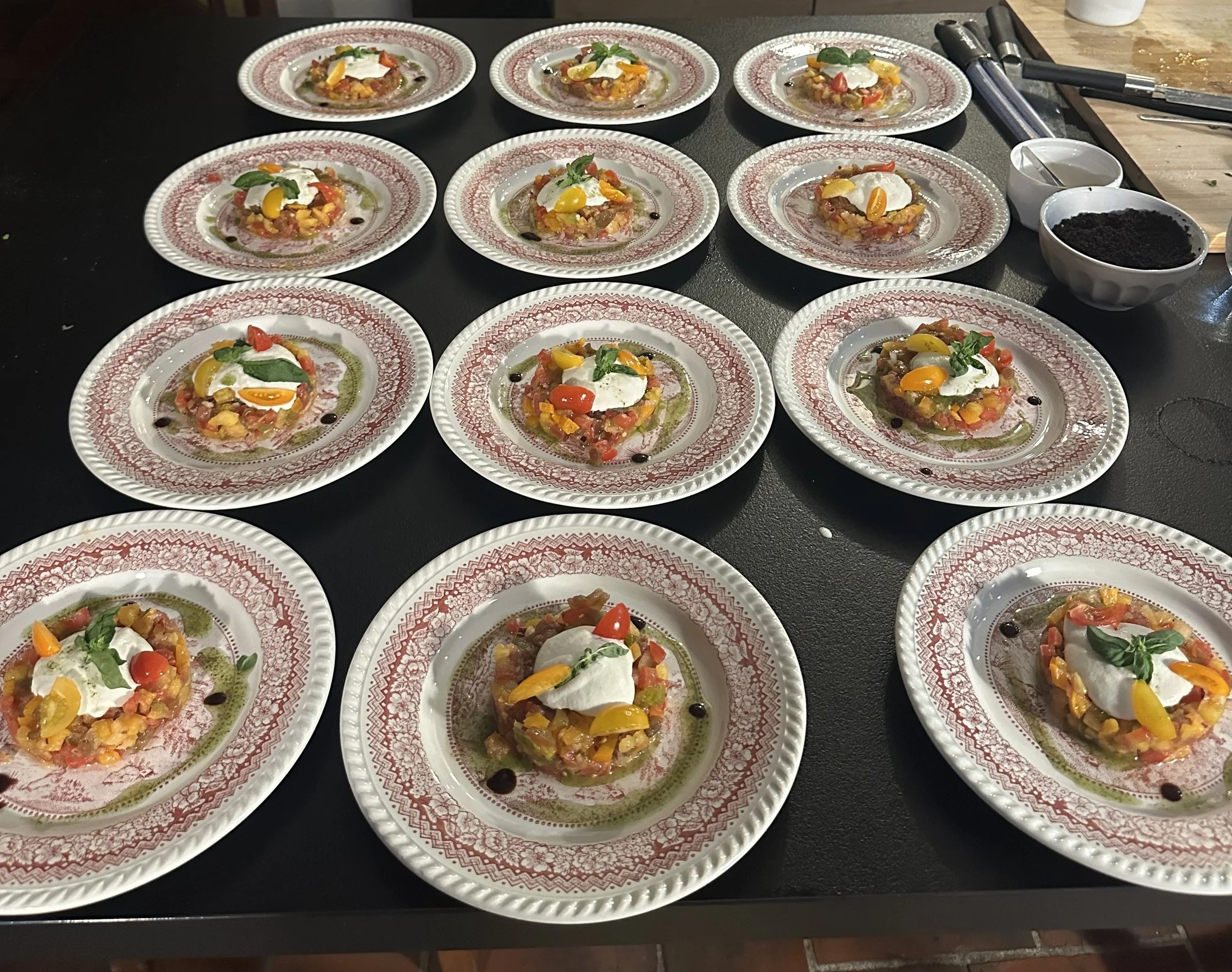 Plate de tartare de poisson, garnie de crème, tomates cerises, basilic, et huile d'olive, sur une table de cuisine.