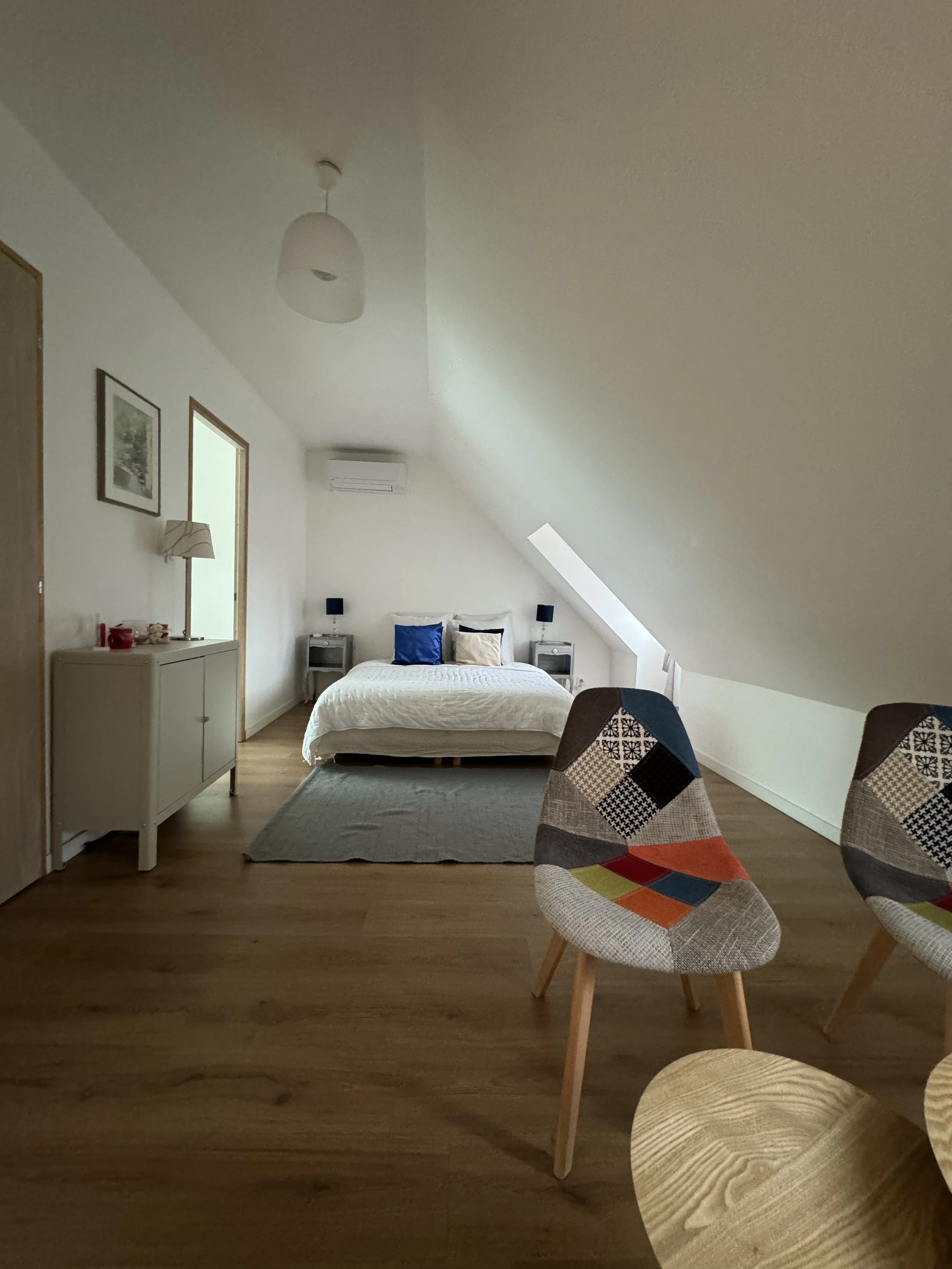 Chambre d'hôtel avec lit double, lampes de lecture, deux tableaux, et deux chaises avec motifs colorés.
