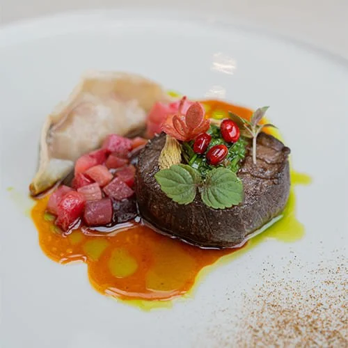 Un plat gastronomique avec un morceau de viande, une pomme de terre farcie, des petits cubes de betterave, et des garnitures végétales et de sauce