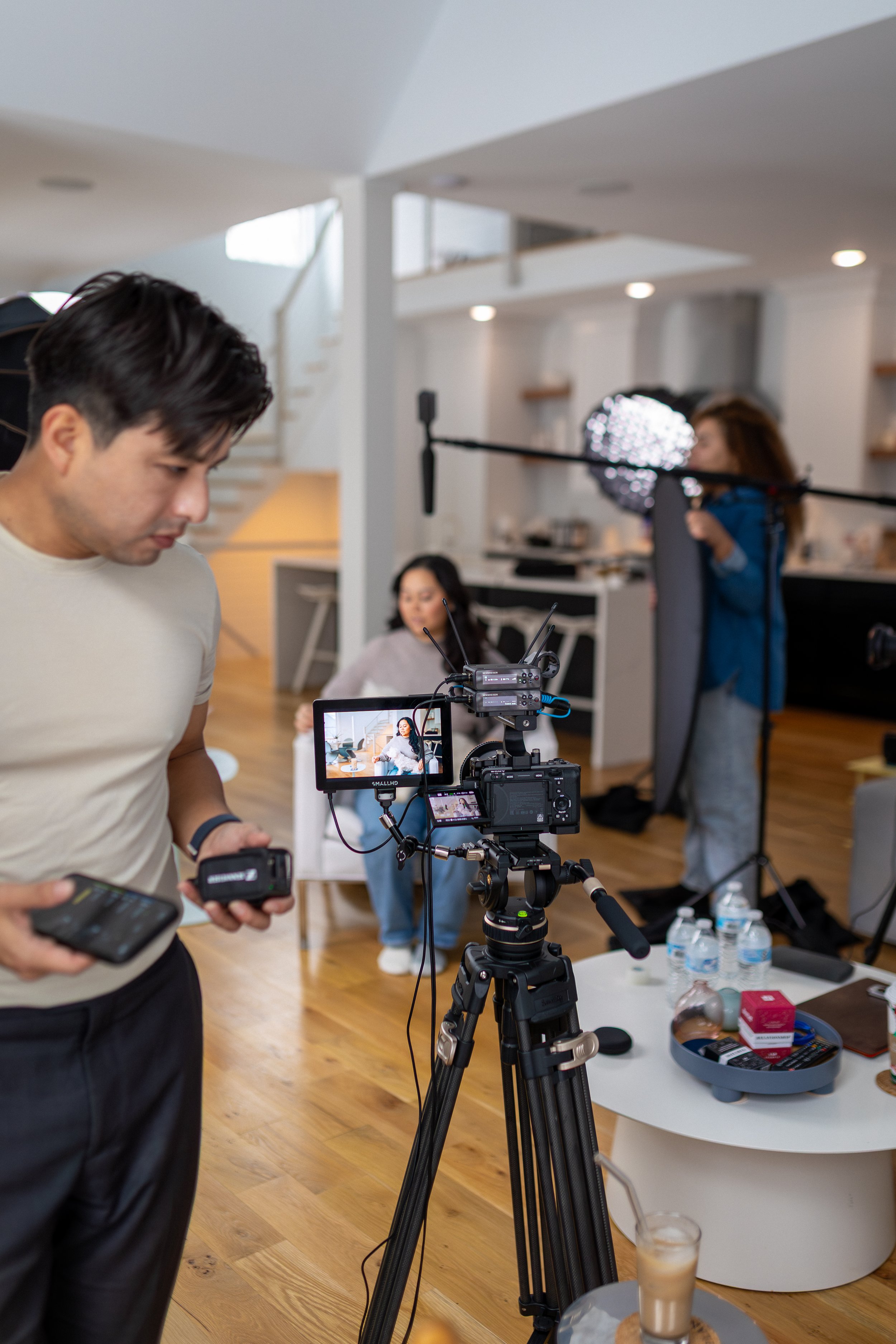 Filming crew setting up camera equipment in a modern living room with a woman seated in the background.