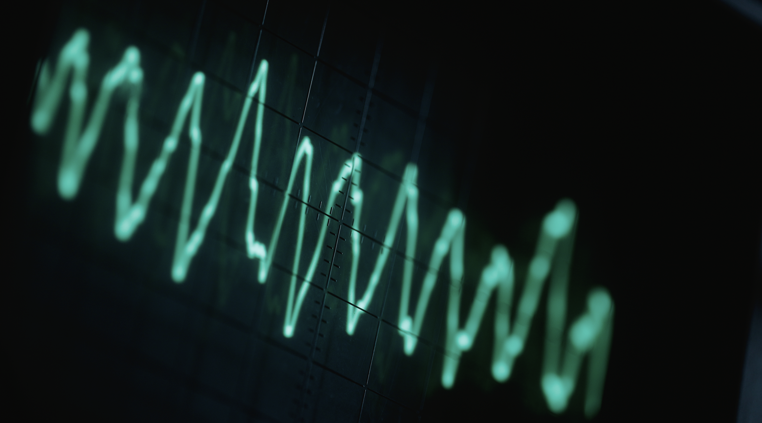 Green oscillating wave on an oscilloscope screen, showing waveform data in low light.