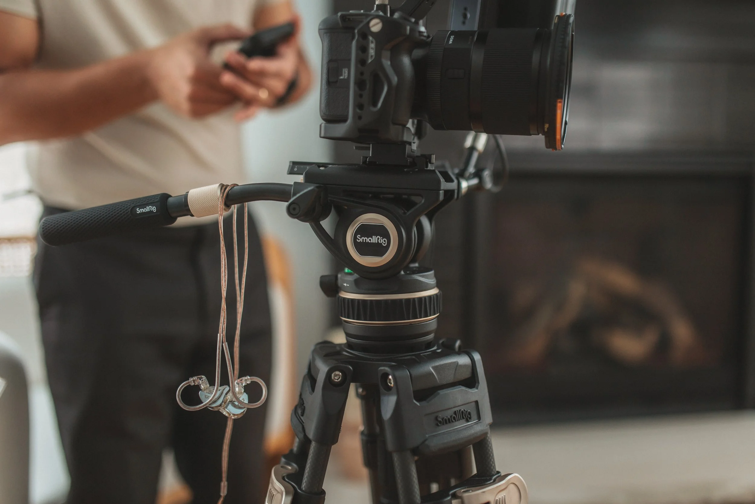 Camera on SmallRig tripod, man holding phone in background.
