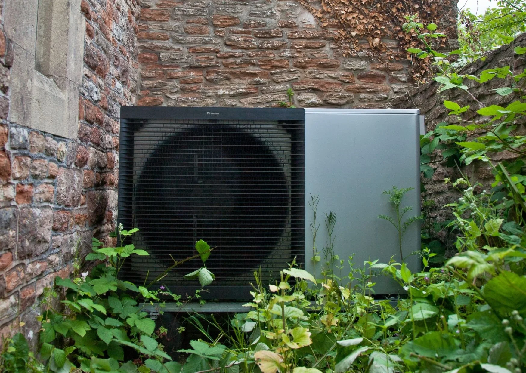Heat pump system outside historic home in Bath with plants growing
