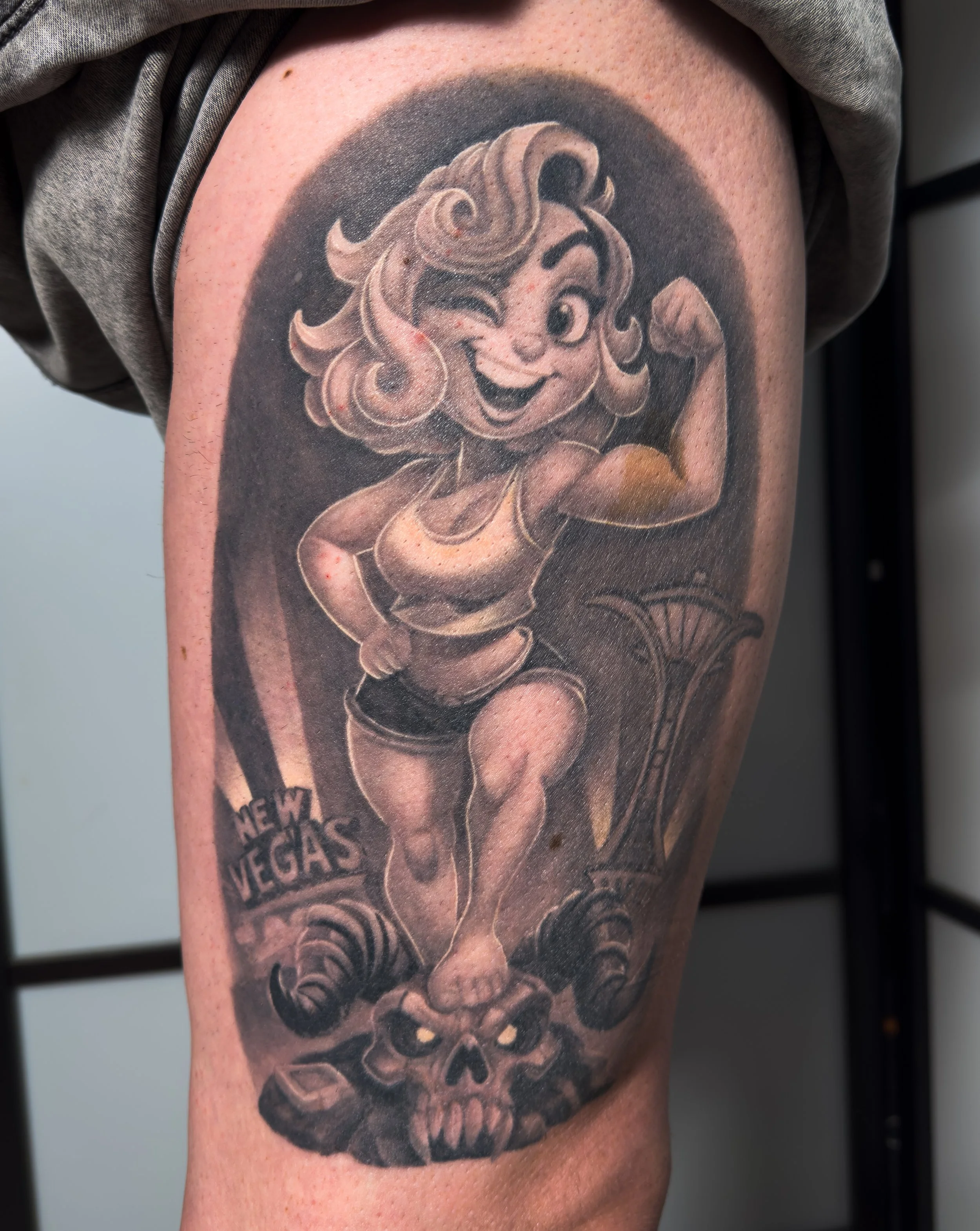 Tattoo of a smiling cartoon girl with curly hair, holding a sandwich, on a person's upper arm with text reading 'New Vegas' below.