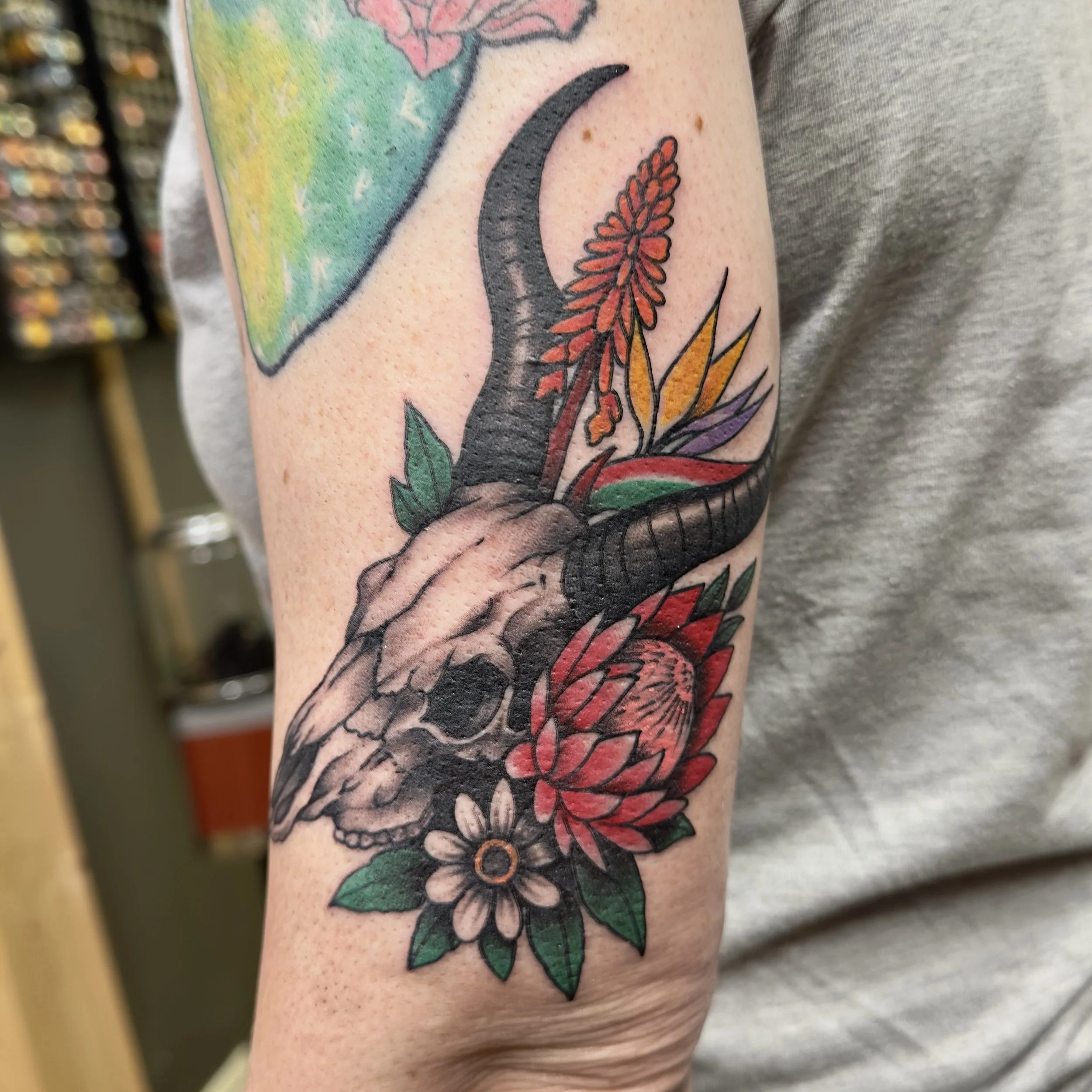 Colorful tattoo of a crescent moon, flowers, and leaves on a person's arm.