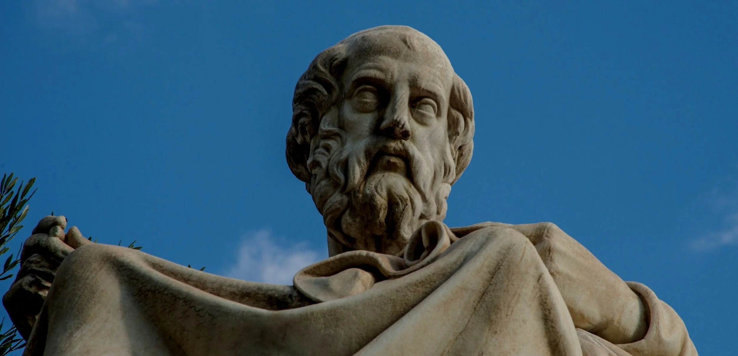 Marble statue of Plato a bearded philosopher against a blue sky.