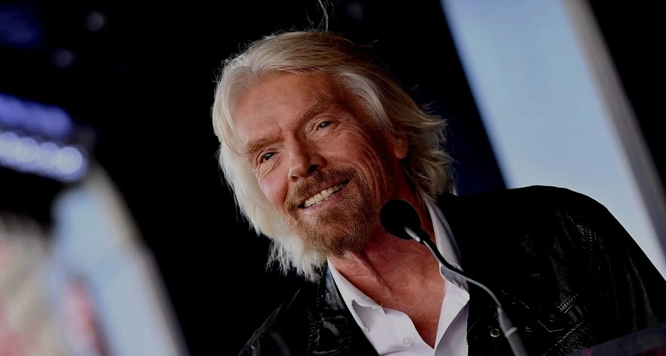 Richard Branson CEO founder with white hair and beard speaking at a microphone