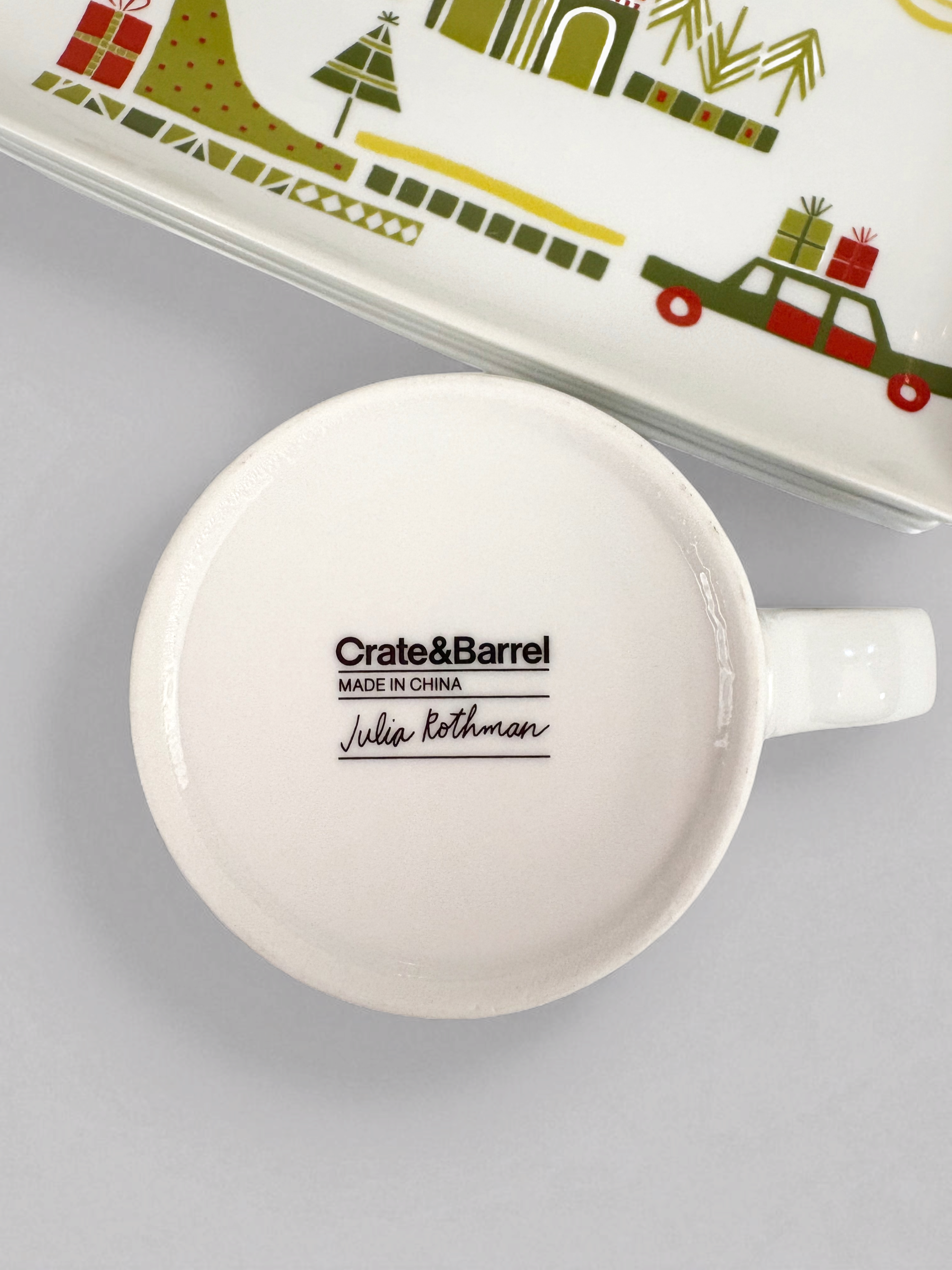 Set of Crate & Barrel Yule Town ceramic holiday plates and mugs by Julia Rothman, featuring whimsical village illustrations.
