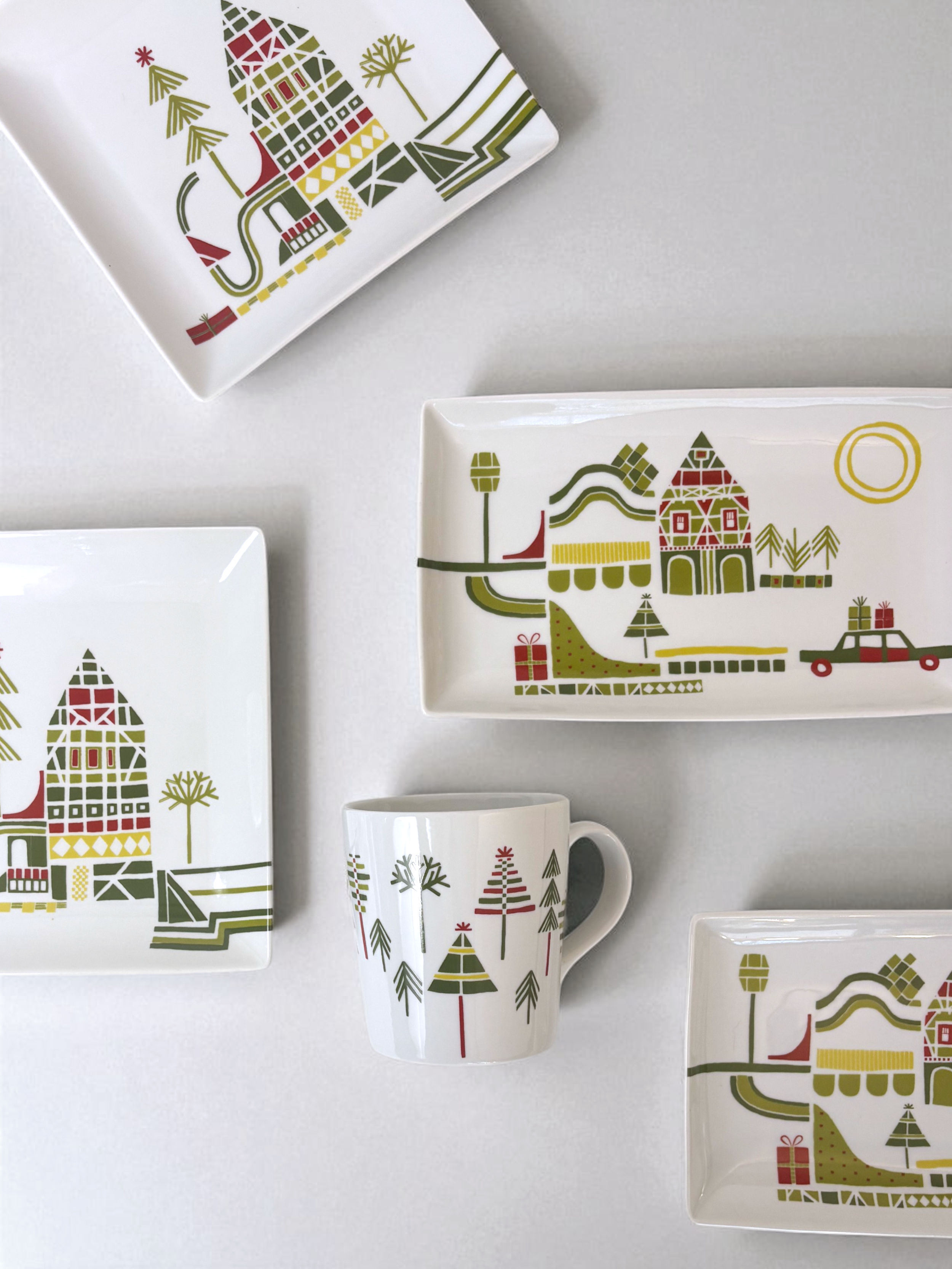 Set of Crate & Barrel Yule Town ceramic holiday plates and mugs by Julia Rothman, featuring whimsical village illustrations.