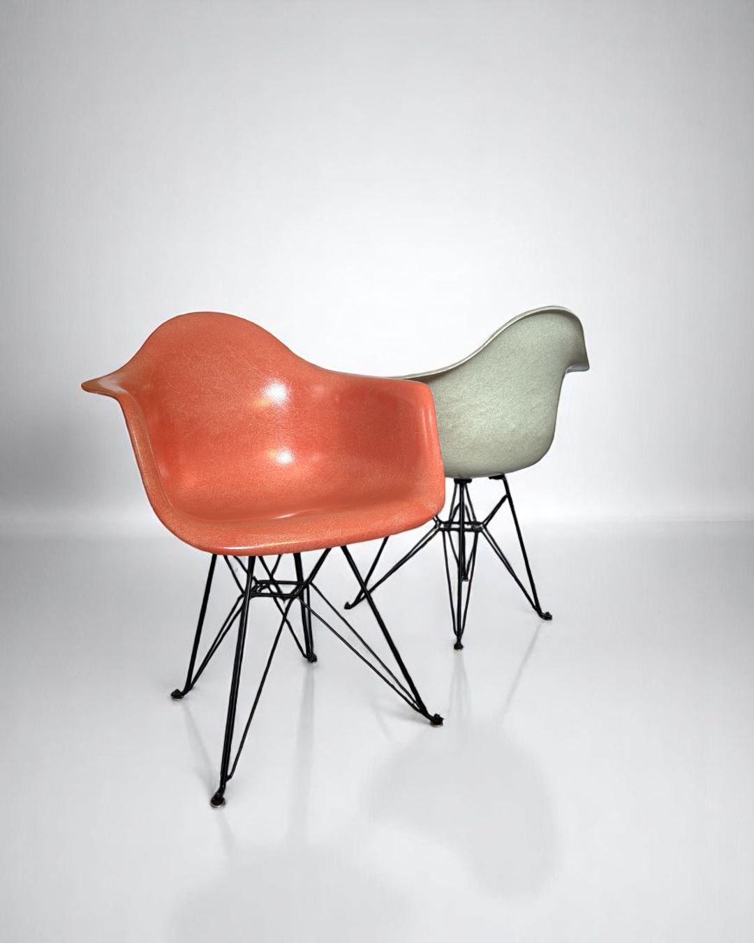 Set of two Modernica Case Study Furniture Arm Shell Eiffel chairs, pre-owned, one coral and one natural, with black metal bases.
