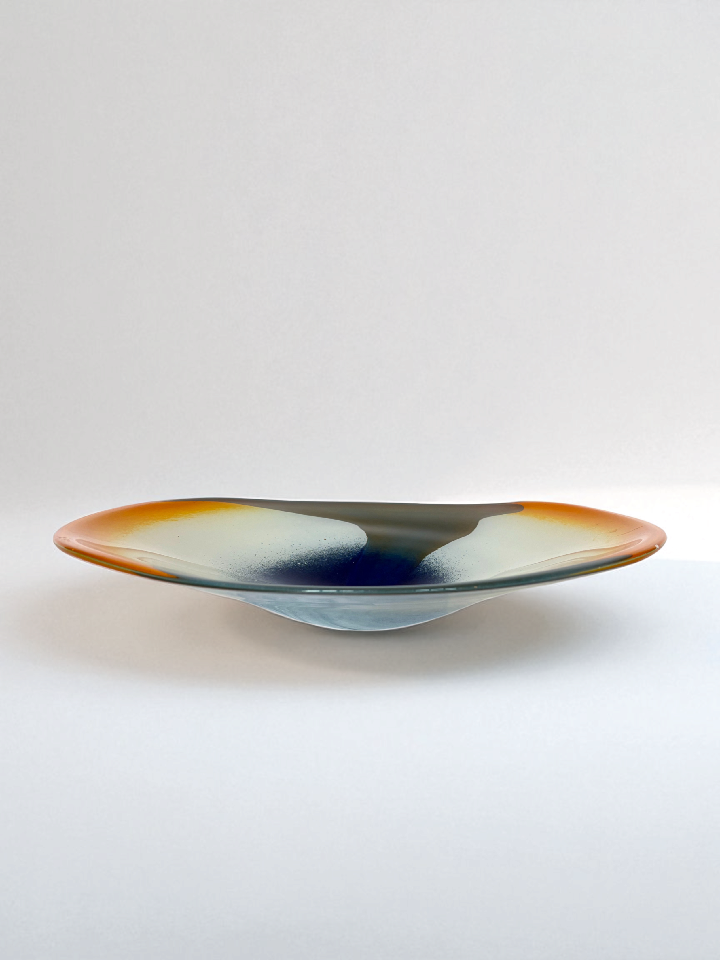 Image of handblown european art glass low bowl/plate. Colors are orange, white, navy and olive green produced in a style similar to nuvo Lithuania.