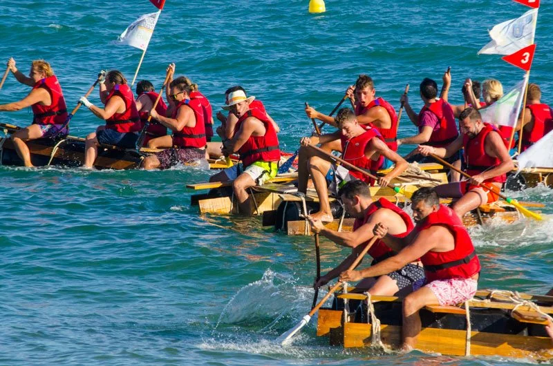 A group of people participating in a dragon boat race on the water, all wearing red life jackets and paddling in unison.