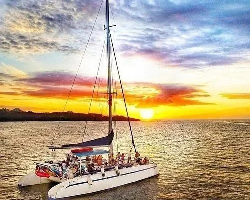 A sailboat with people on board floating on a body of water during a colorful sunset.