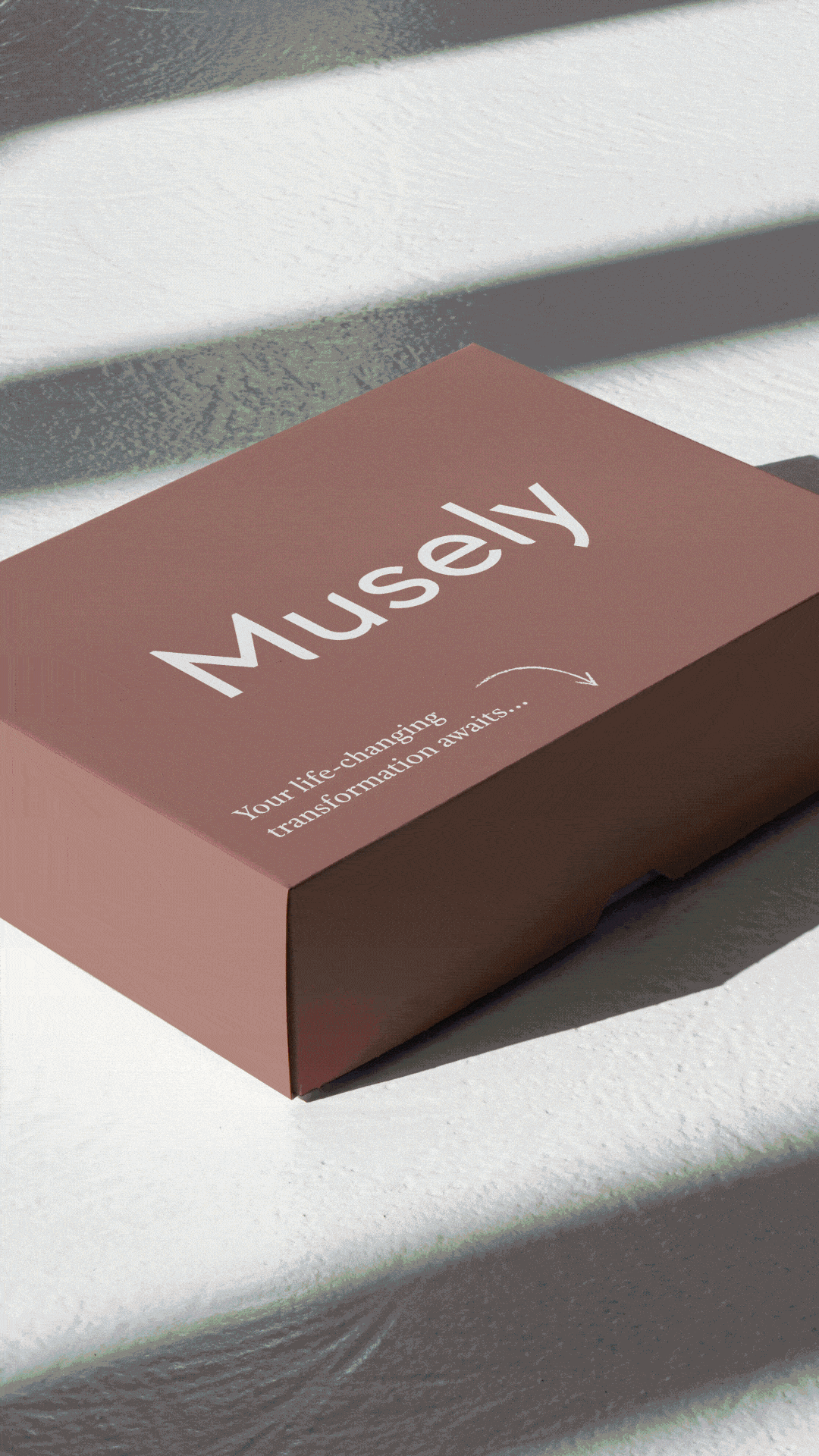 A pink box labeled 'Musely' with the tagline 'Your life-changing transformation awaits...' is sitting on a textured white surface, casting soft shadows from overhead lighting.