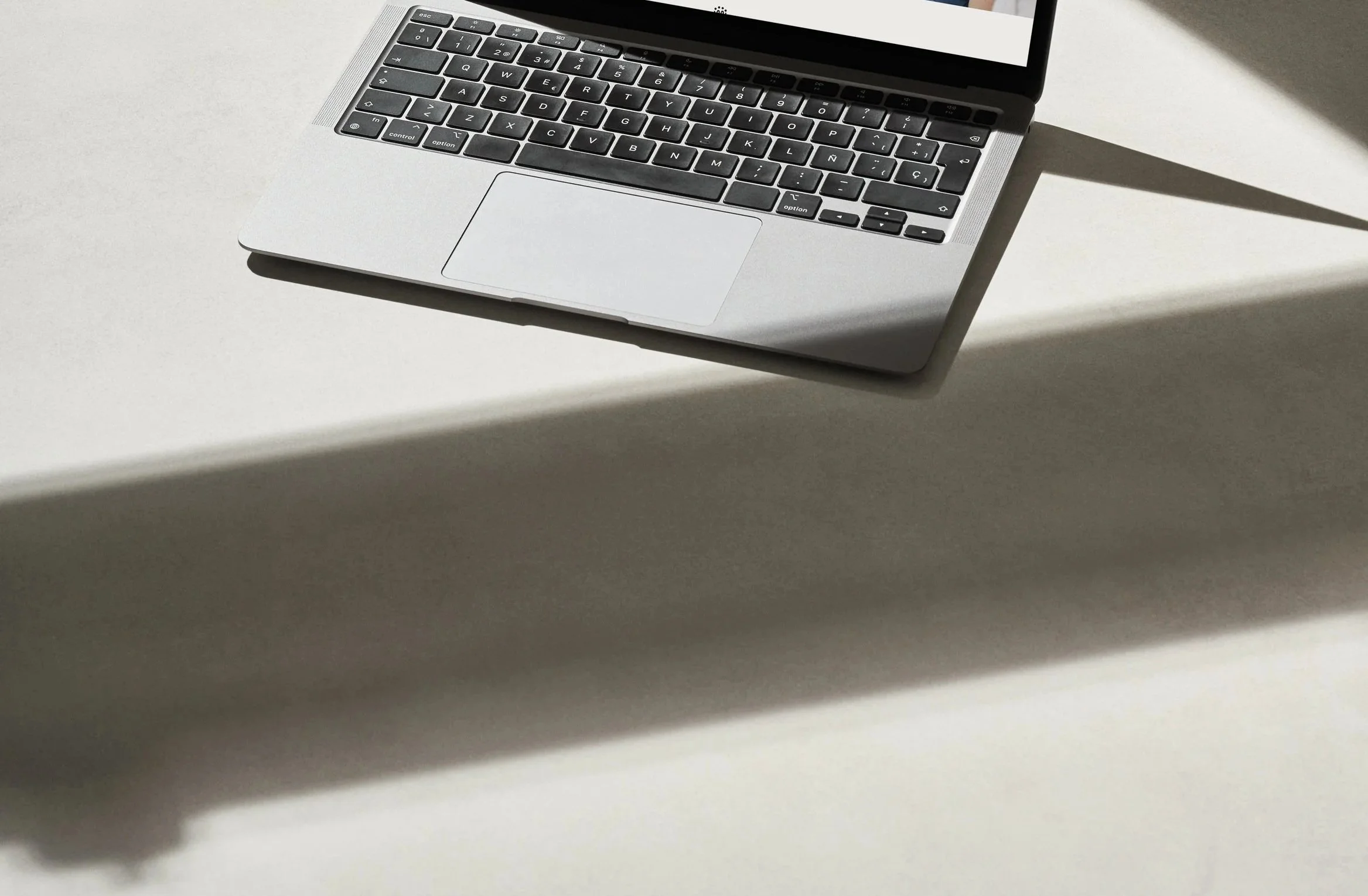 A laptop computer with a black keyboard is placed on a white surface, casting a shadow.