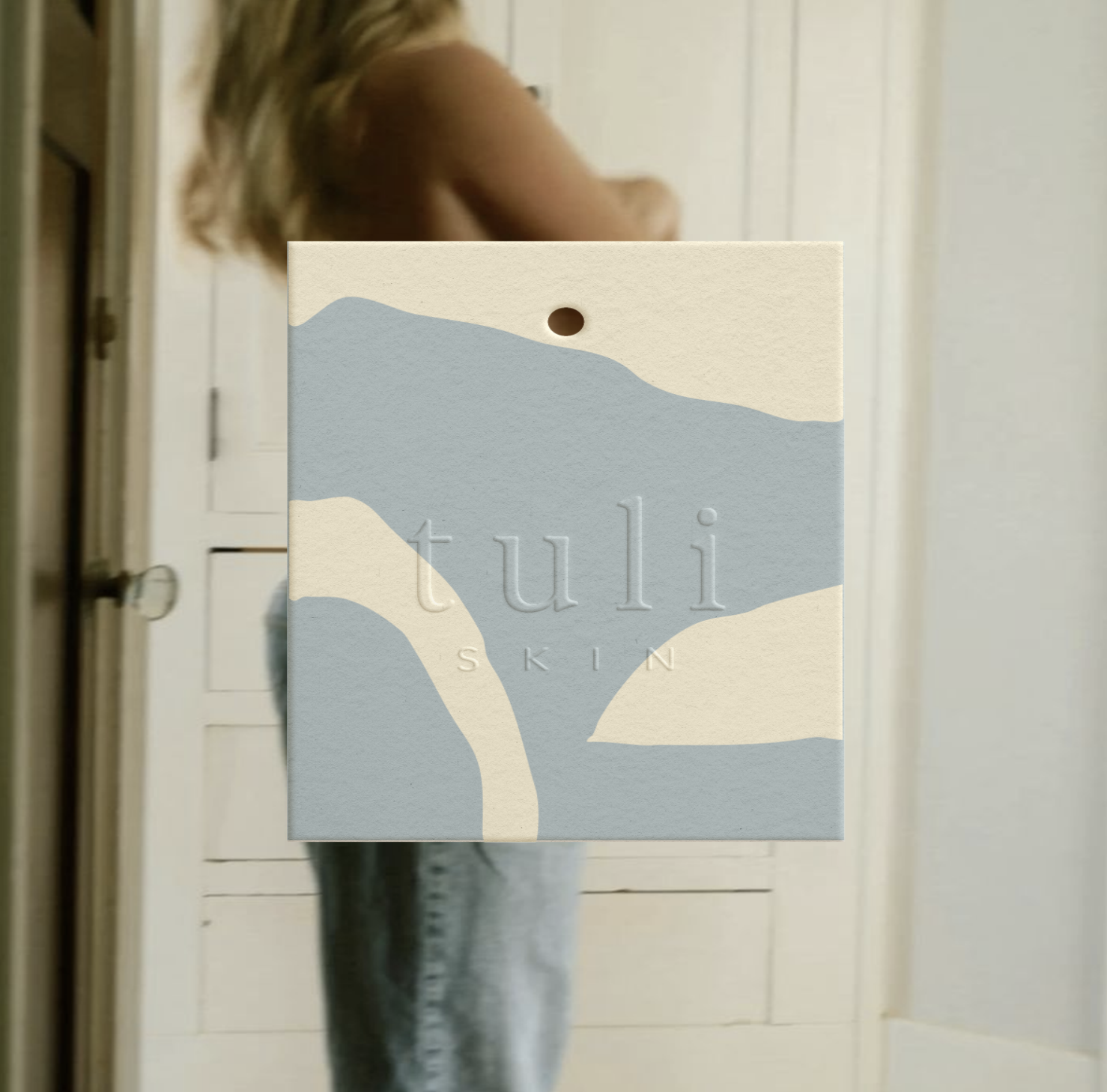 A person taking a mirror selfie with a product box in front of their face, the box has the text 'fuli SKIN' on it, and the background shows a door and a white wall.