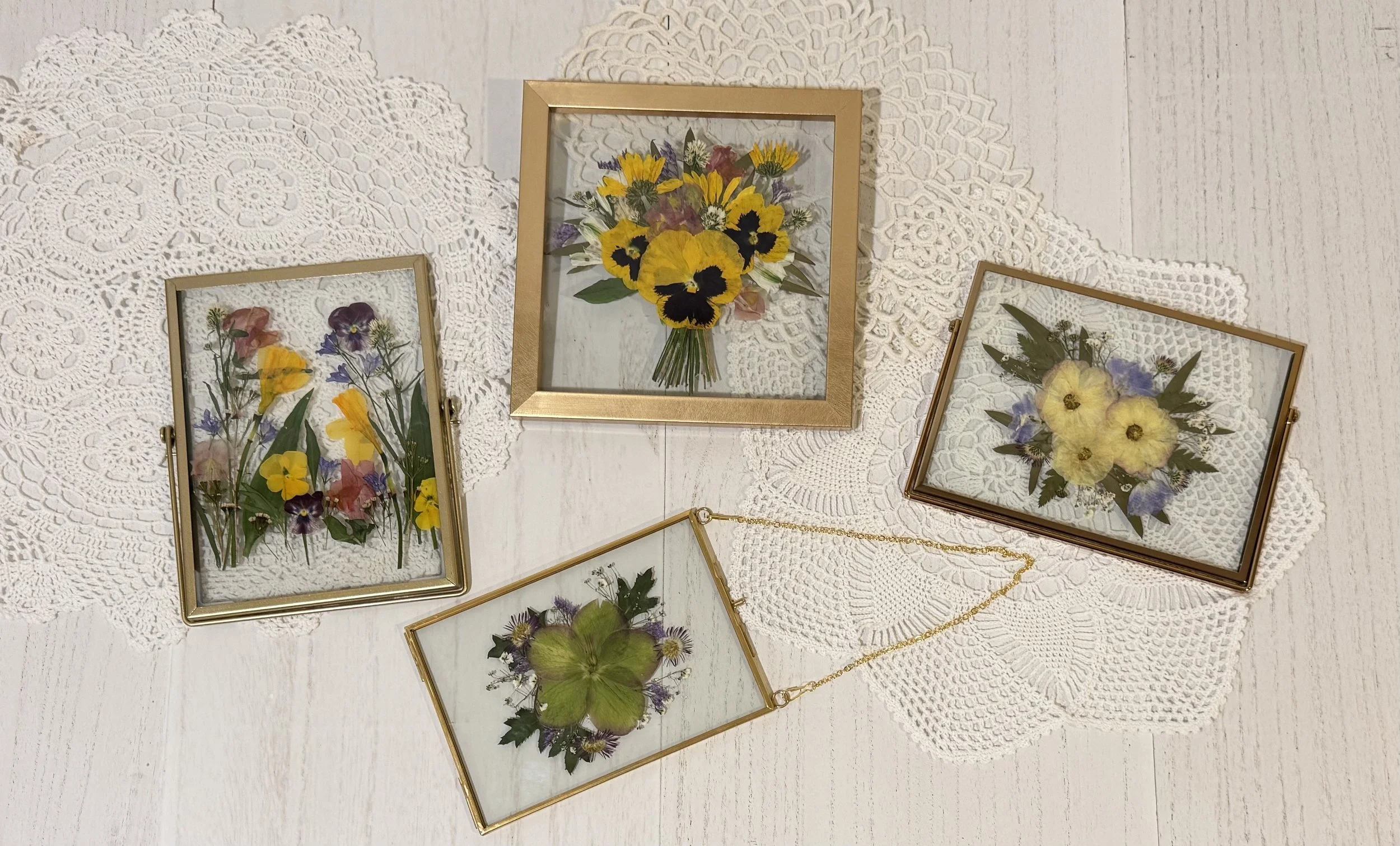 Pressed flower artworks in brass frames on lace doilies.